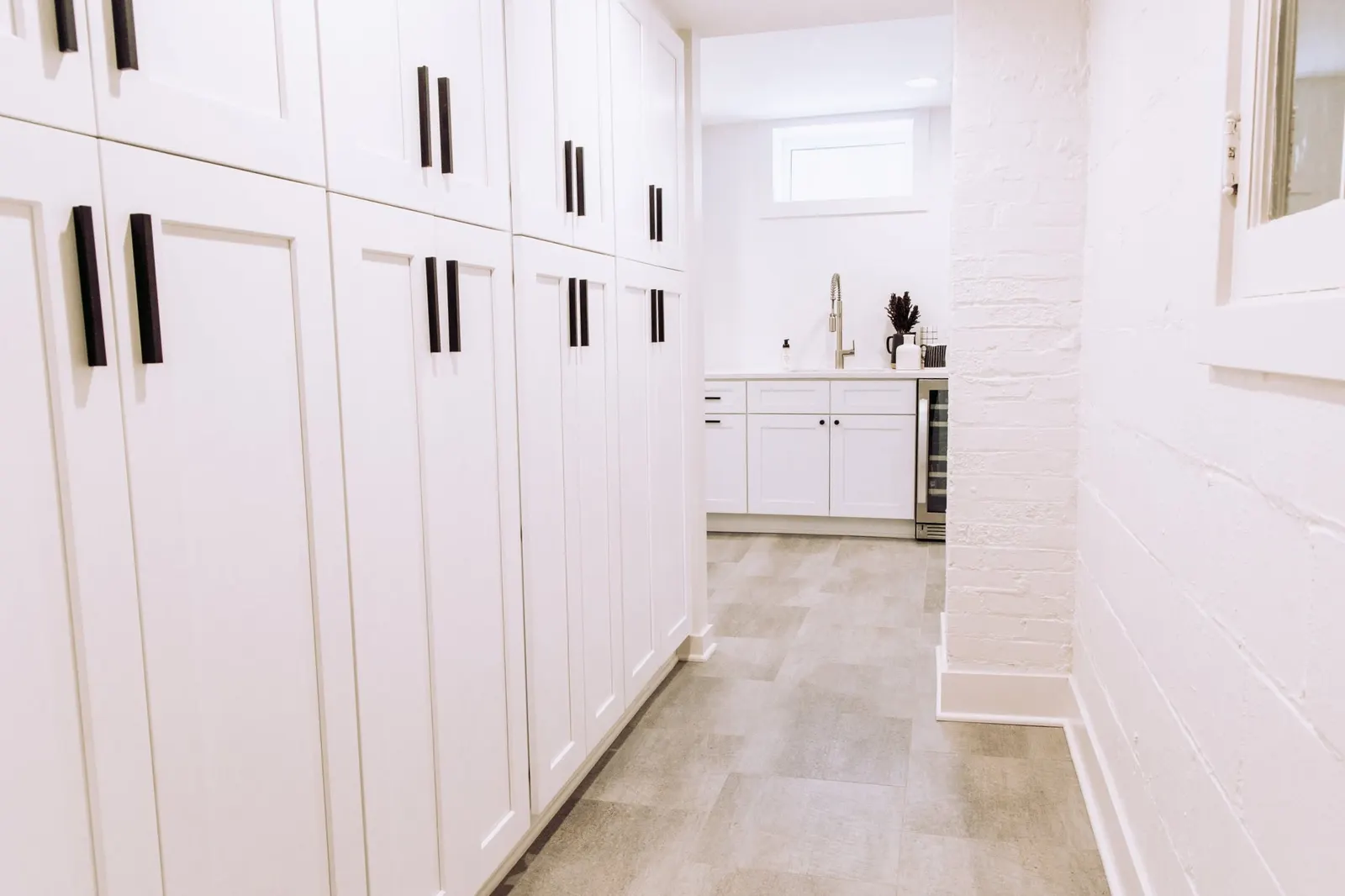 1922 Basement Remodel, laundry room, white cabinets, matte black hardware, brushed nickel faucet, under mount sink, tile floors, beverage fridge, custom cabinetry, Lincoln Nebraska, professional contractors, craftsmanship, storage solutions.