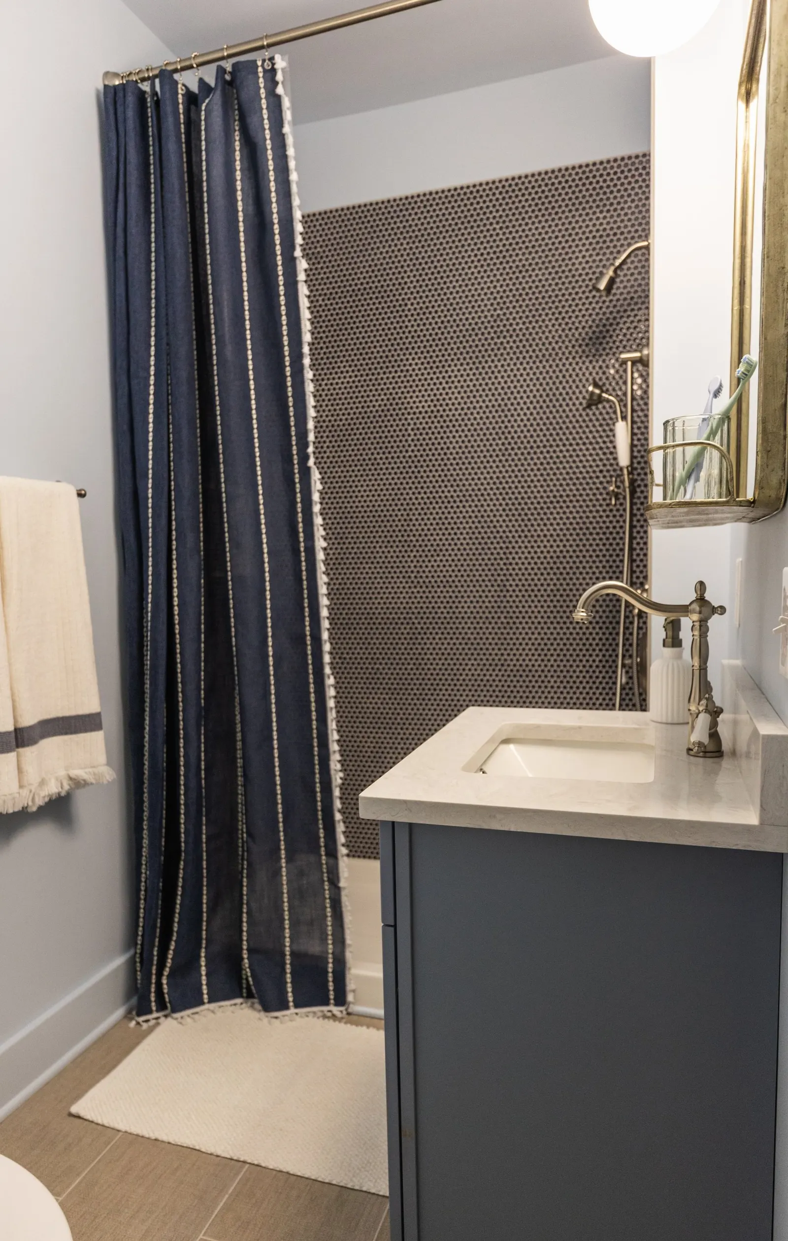 Modern bathroom with navy blue shower curtain, hexagonal tile wall in the shower, wall-mounted shower fixtures, white countertop sink, and beige floor tiles.