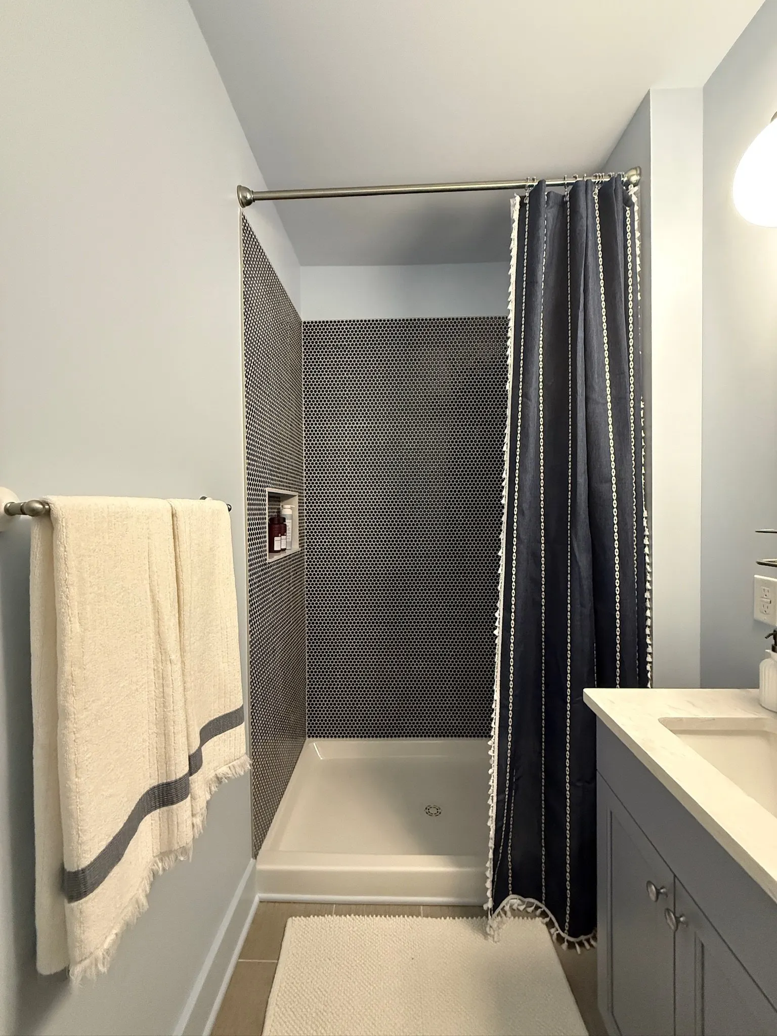 Bathroom with a tiled shower, dark shower curtain, towel on a rack, and a sink with a cabinet.