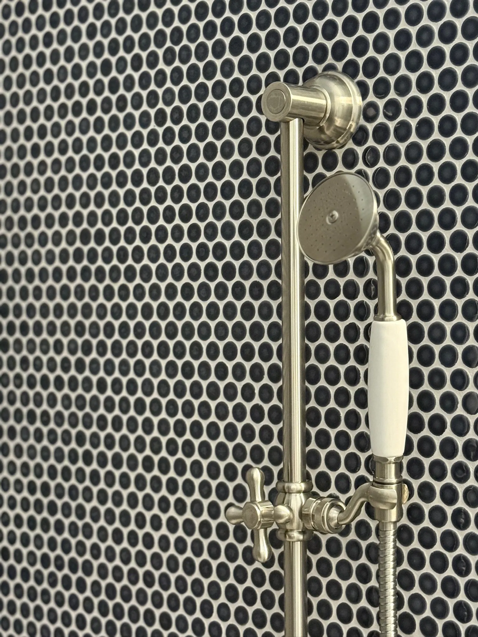 Close-up of a mounted showerhead and handle against a wall with circular black and white tiles.