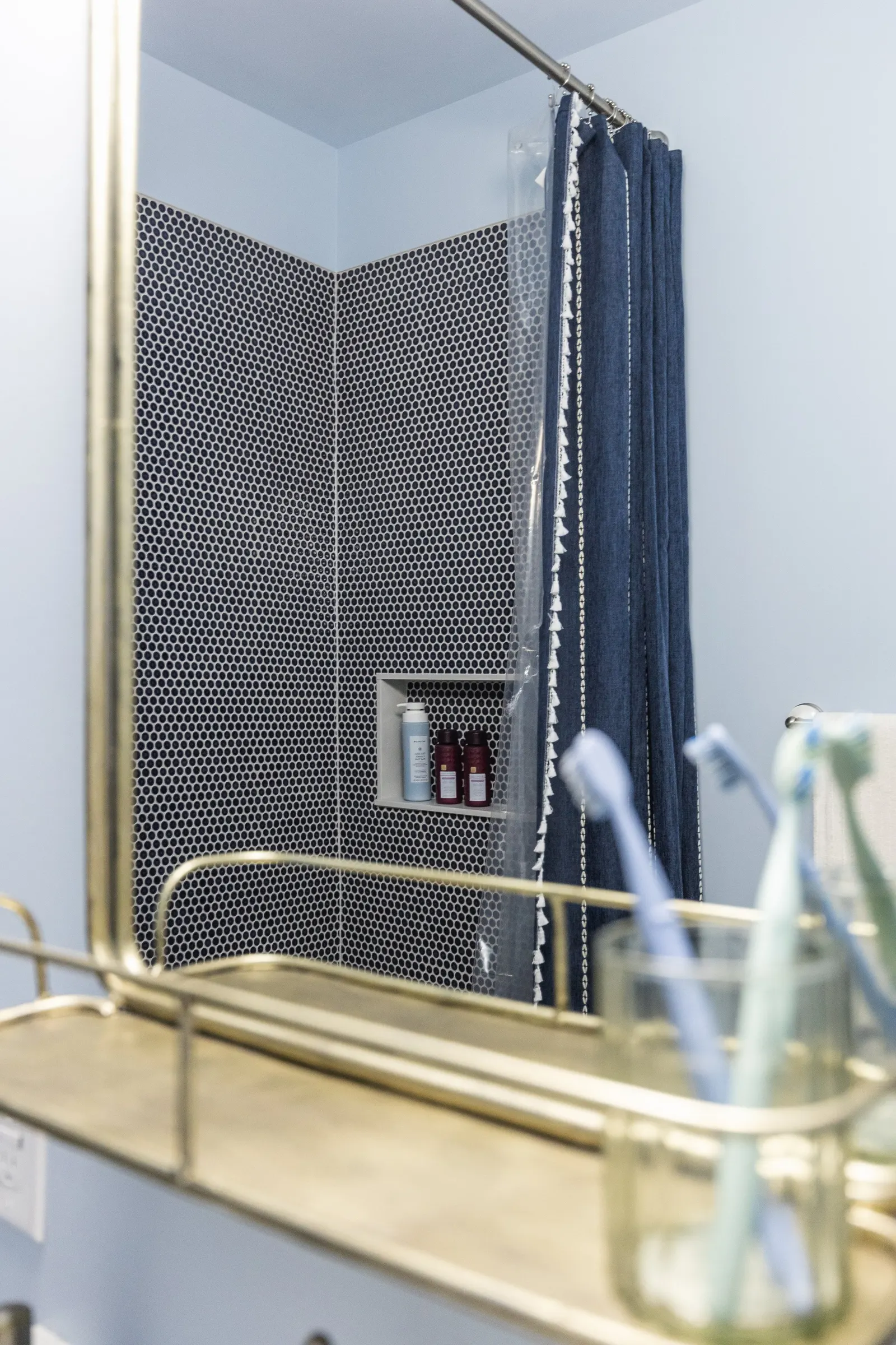 A bathroom shower area with navy blue curtains, black and white hexagonal tile, and a built-in niche with shampoo and body wash bottles.