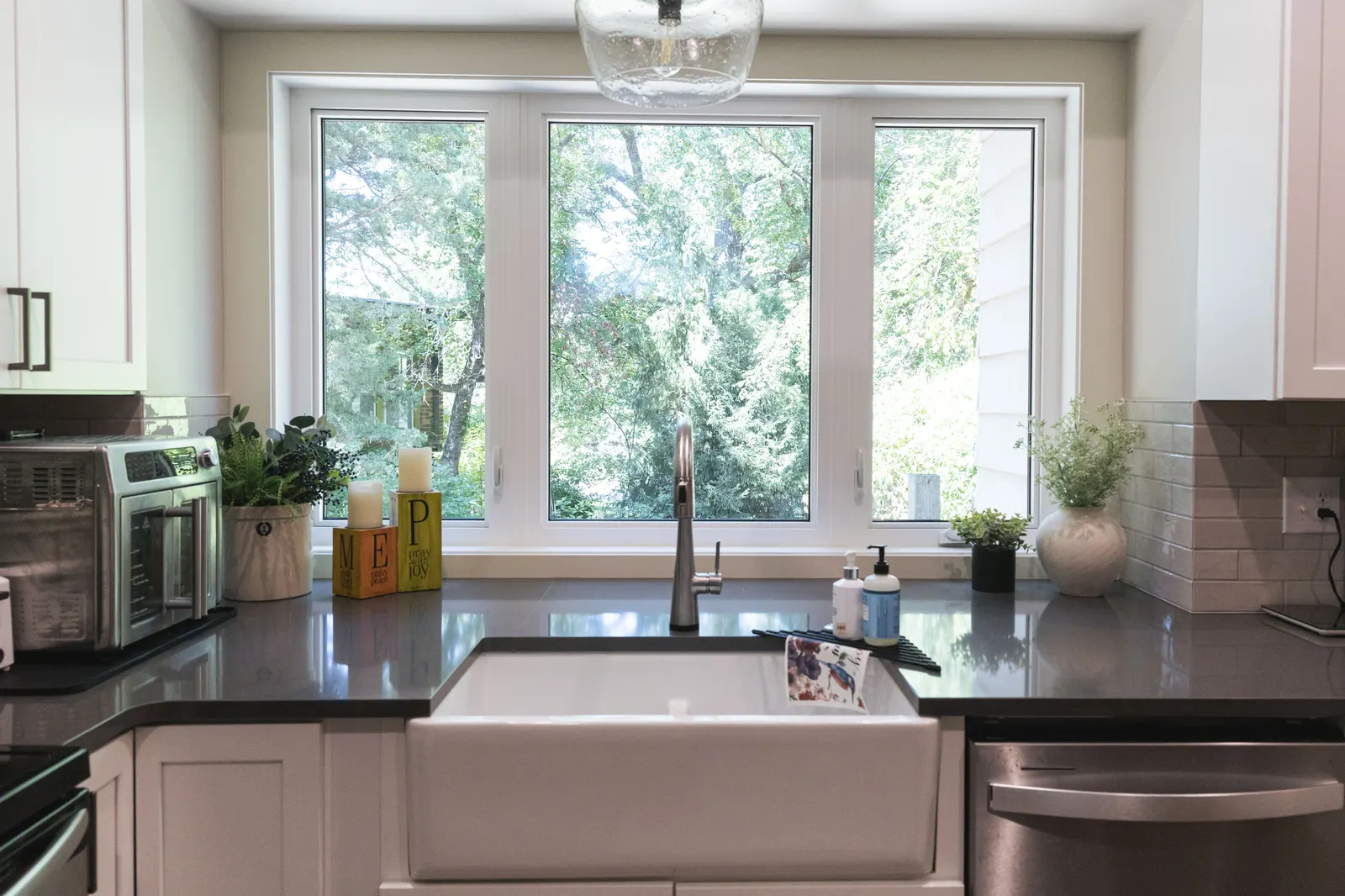 A three-panel bay window over a white fireclay sink, with the quartz countertop running all the way into the window.