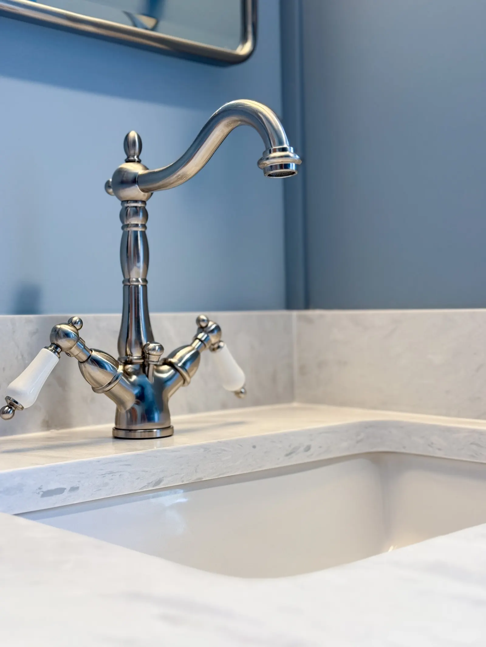A stainless steel kitchen faucet mounted on a light-colored marble sink.
