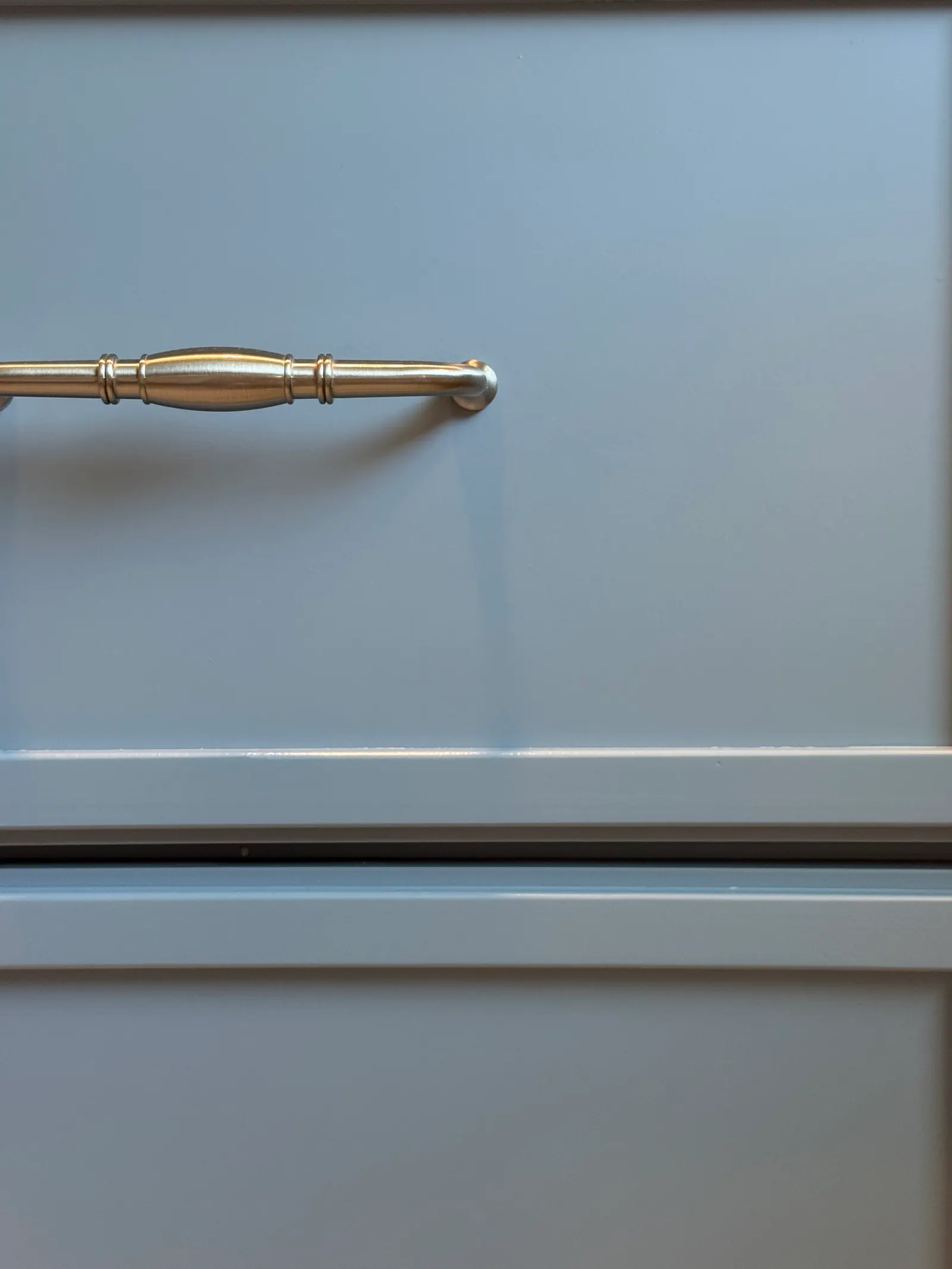 Close-up of a light blue kitchen cabinet drawer with a silver handle.