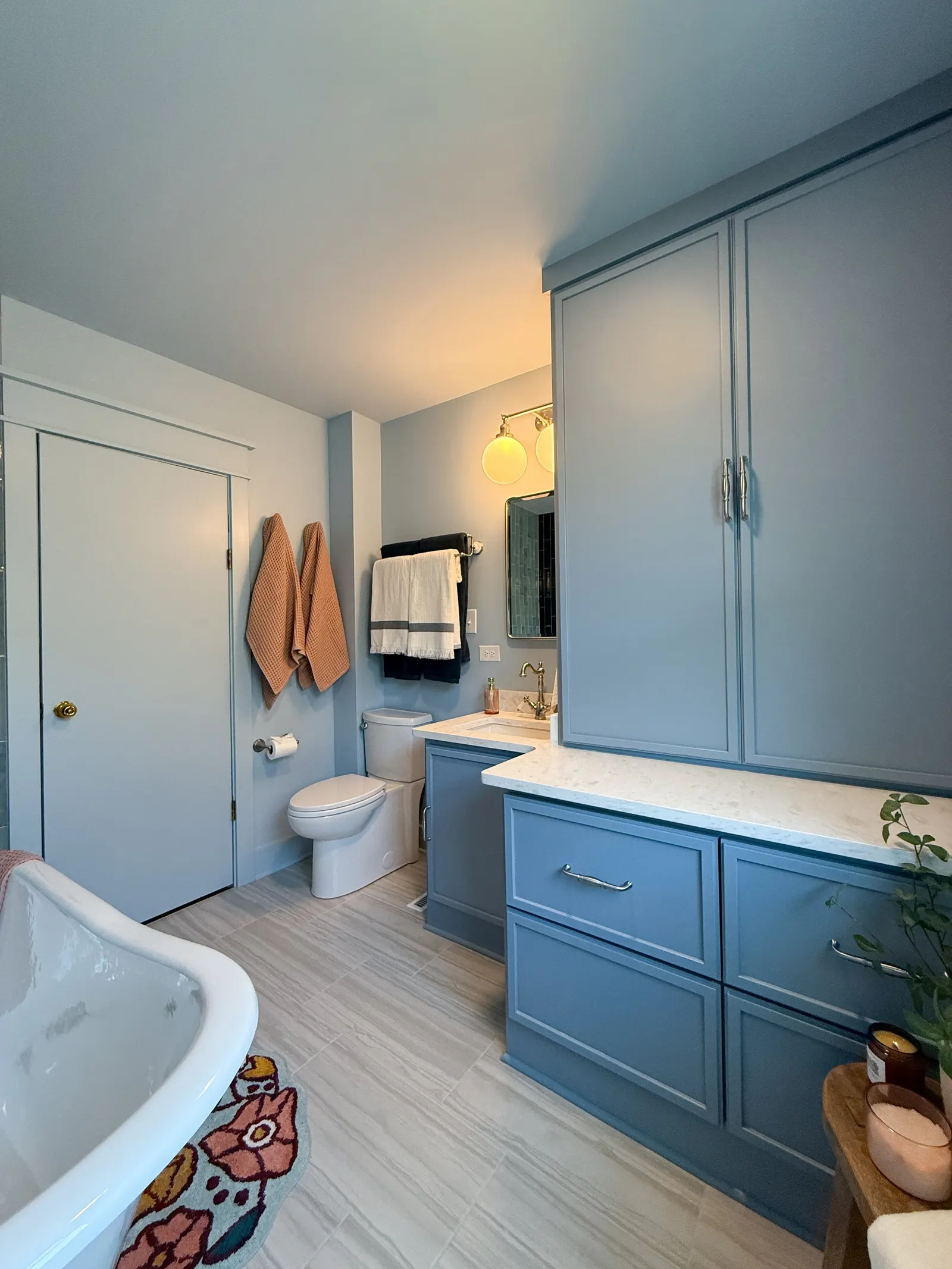 A bathroom with a blue cabinet and a white countertop, a white toilet, a bathtub, and colorful towels hanging on the wall.