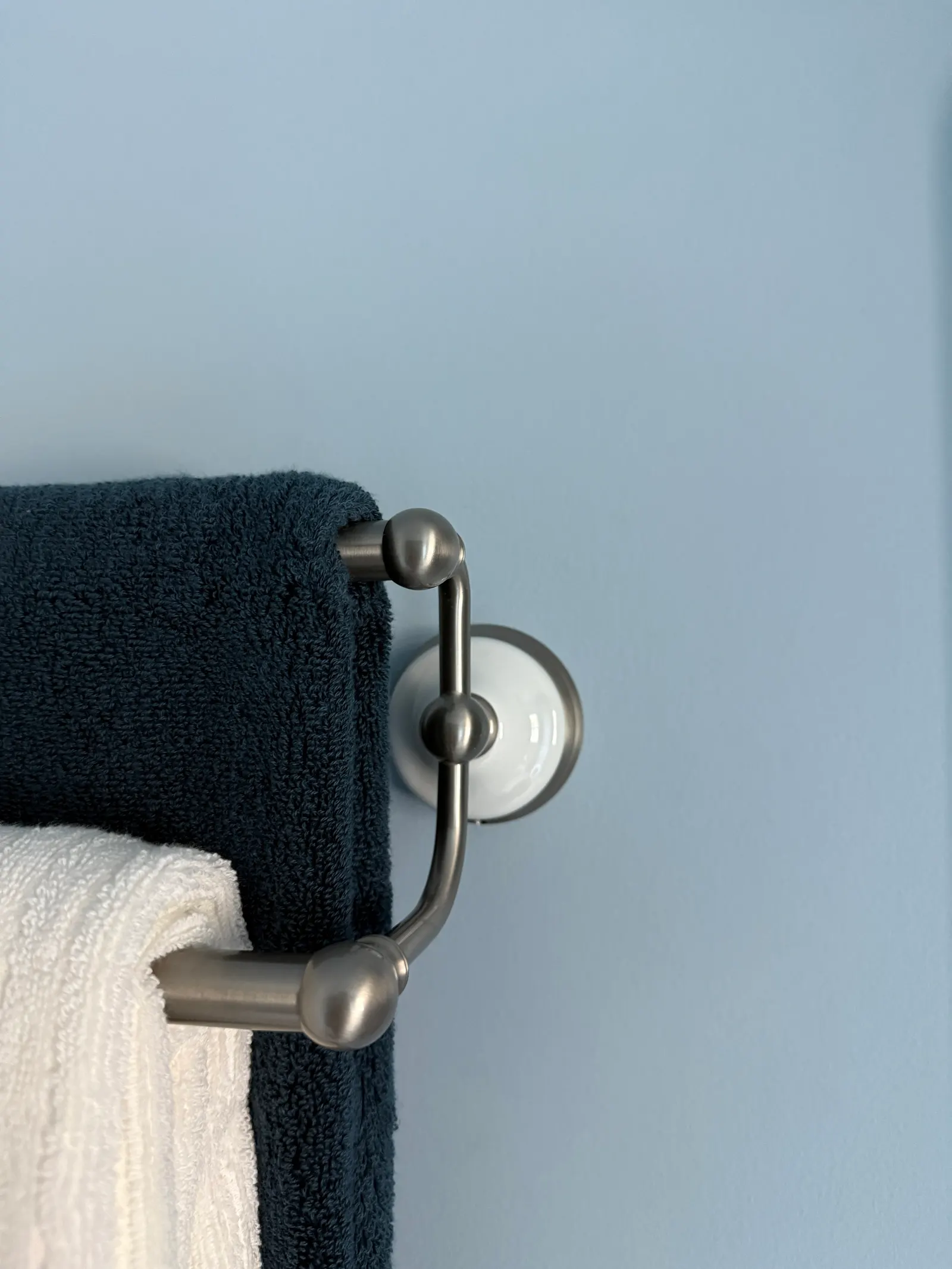 Close-up of a blue towel and a white towel hanging on a metal towel rack on a light blue wall.