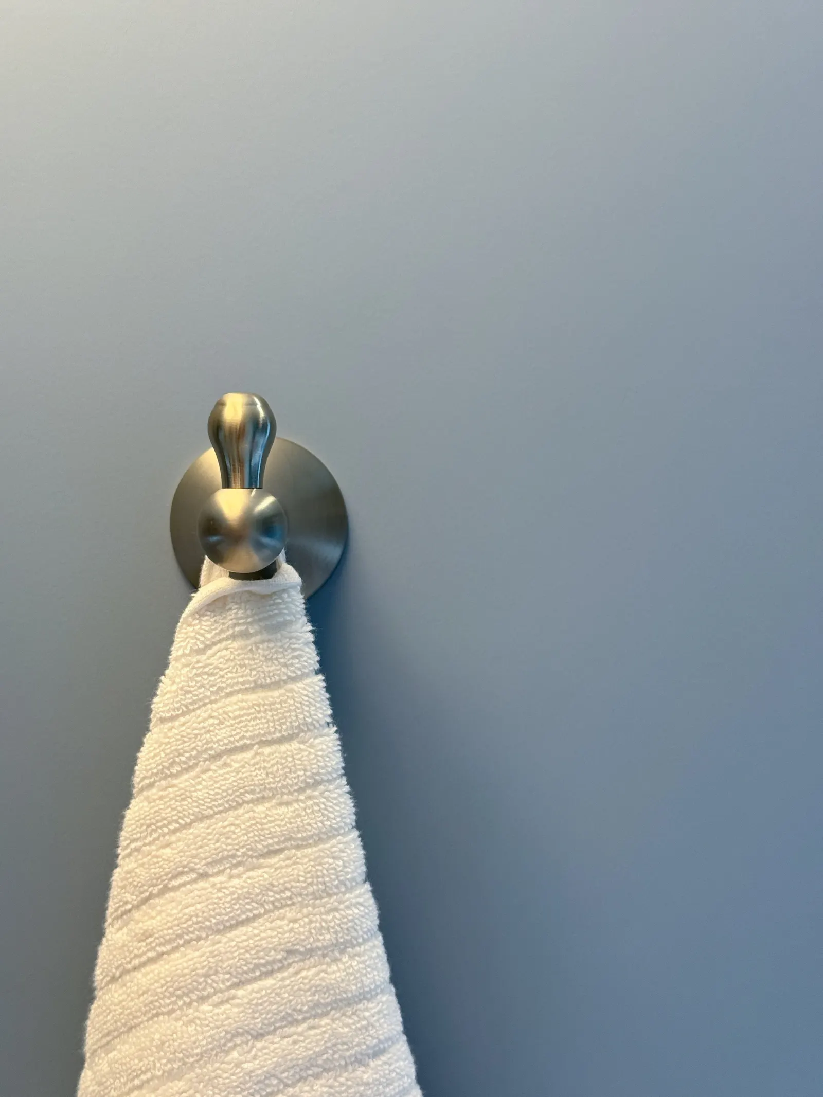 A white towel hanging on a metallic towel hook mounted on a gray wall.
