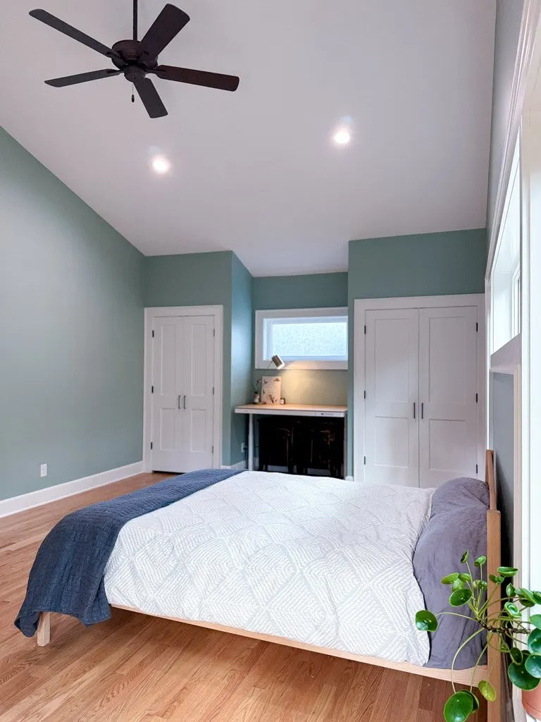 A bedroom with a bed, nightstand, closet, ceiling fan, and a small window.