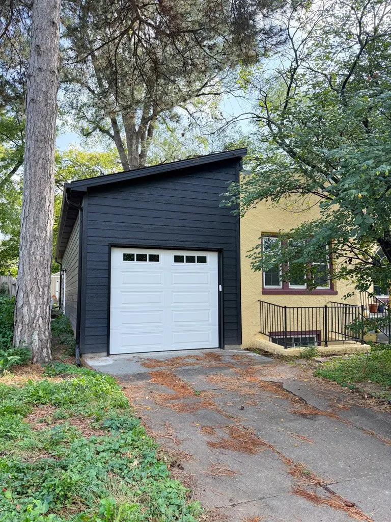A house with a black garage and a white garage door, surrounded by trees and greenery.
