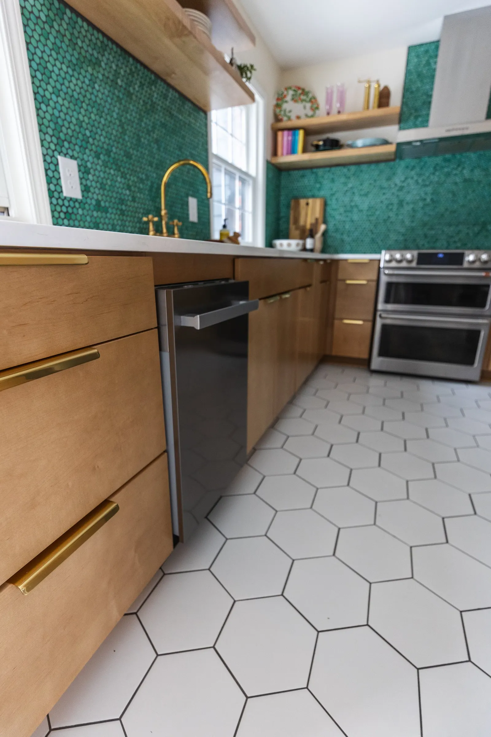 Kitchen with wooden cabinets, white hexagon tiled floor, green tiled backsplash, gold faucet, and stainless steel oven.
