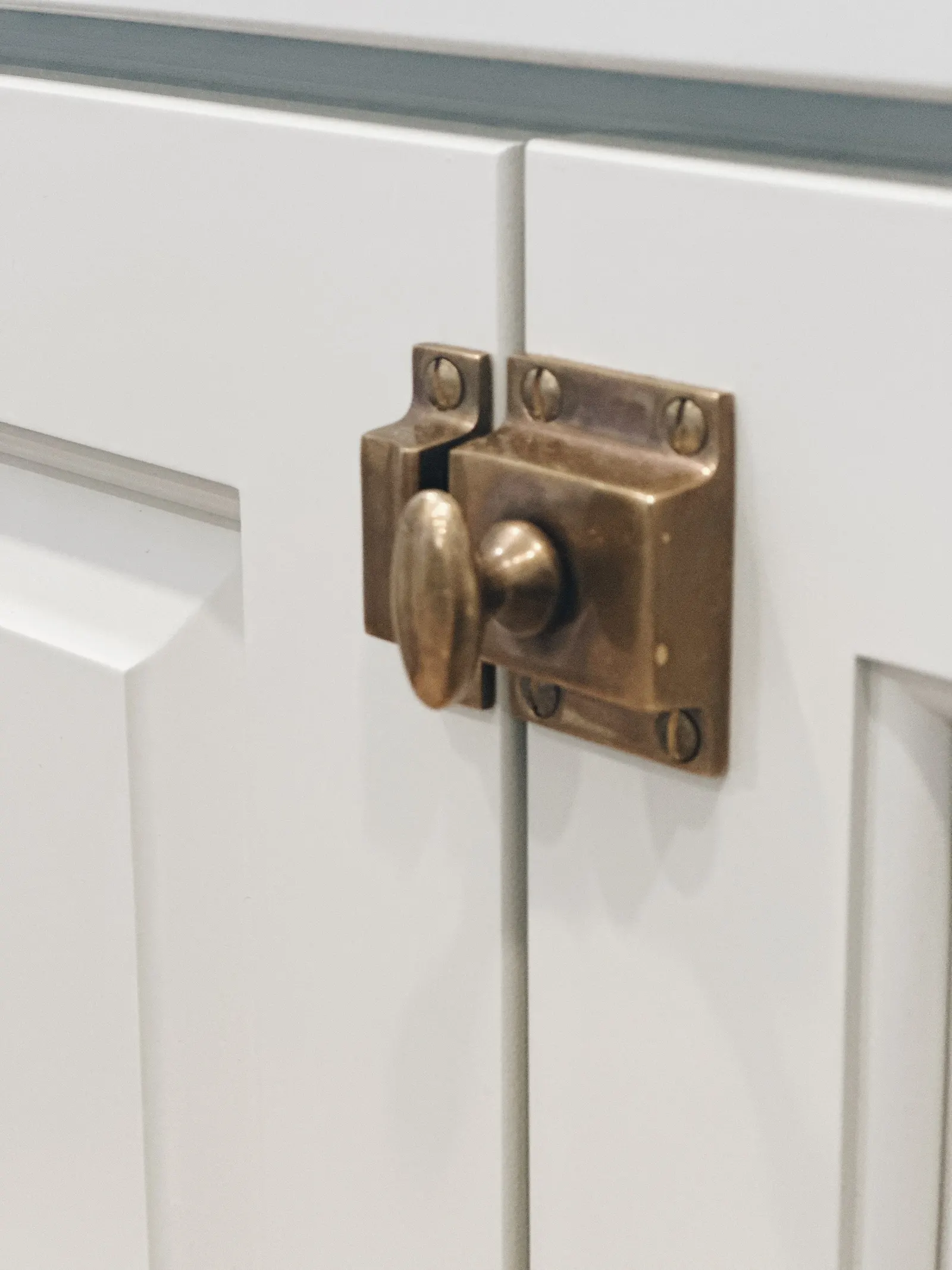 Close-up of a brass latch on a white cabinet door.