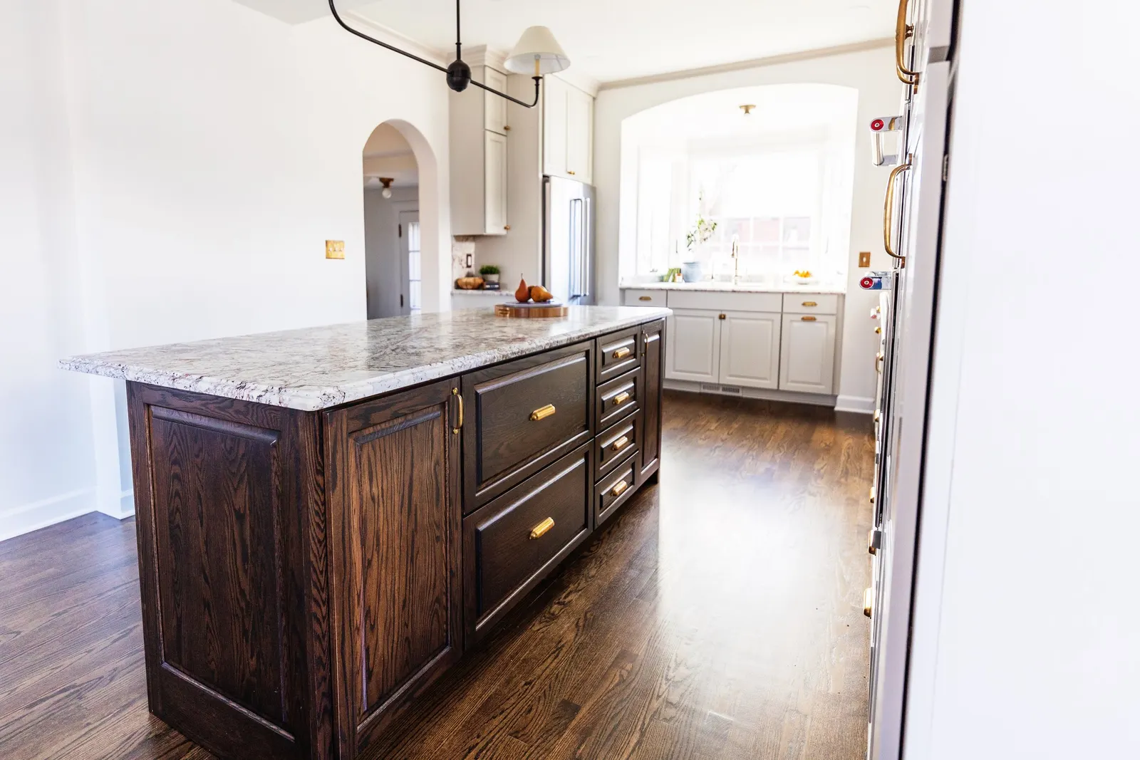 Kitchen with white and dark wood cabinets, a granite countertop island, hardwood floors, and a large window letting in natural light.
