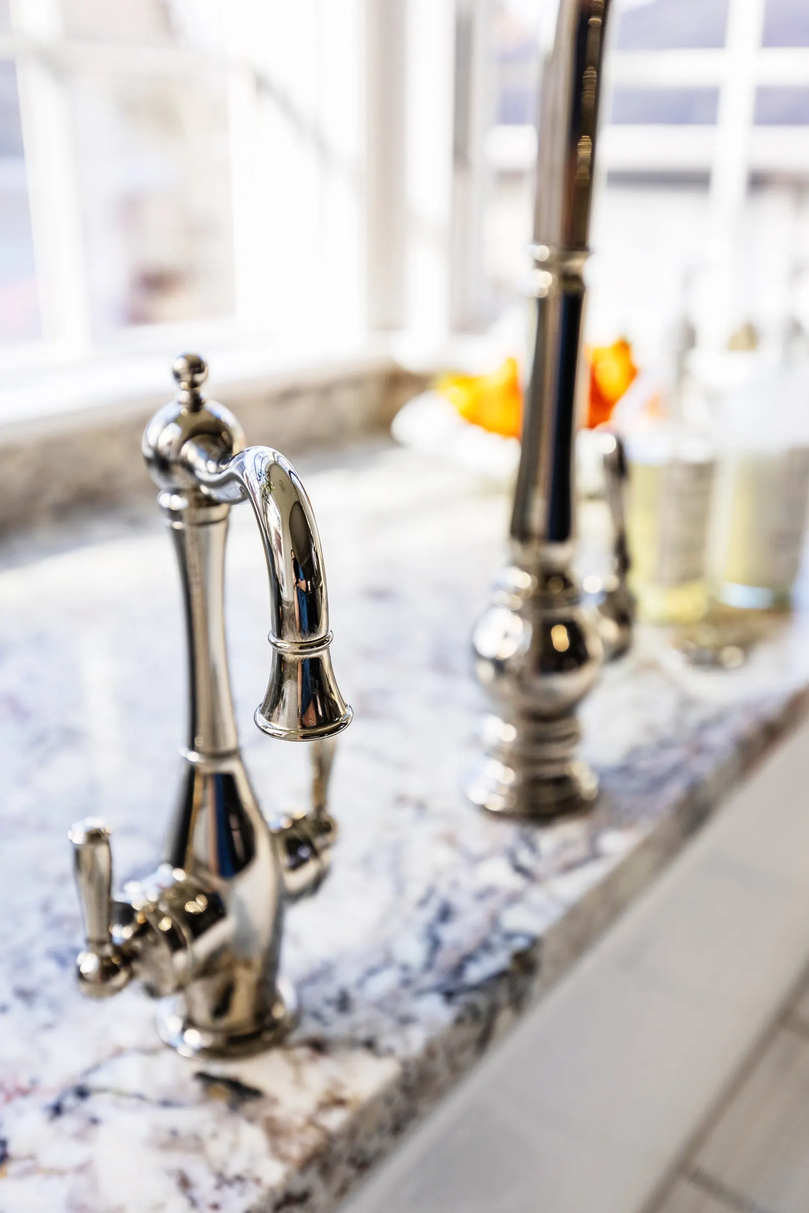 Close-up of a shiny chrome kitchen faucet on a granite countertop near a window.