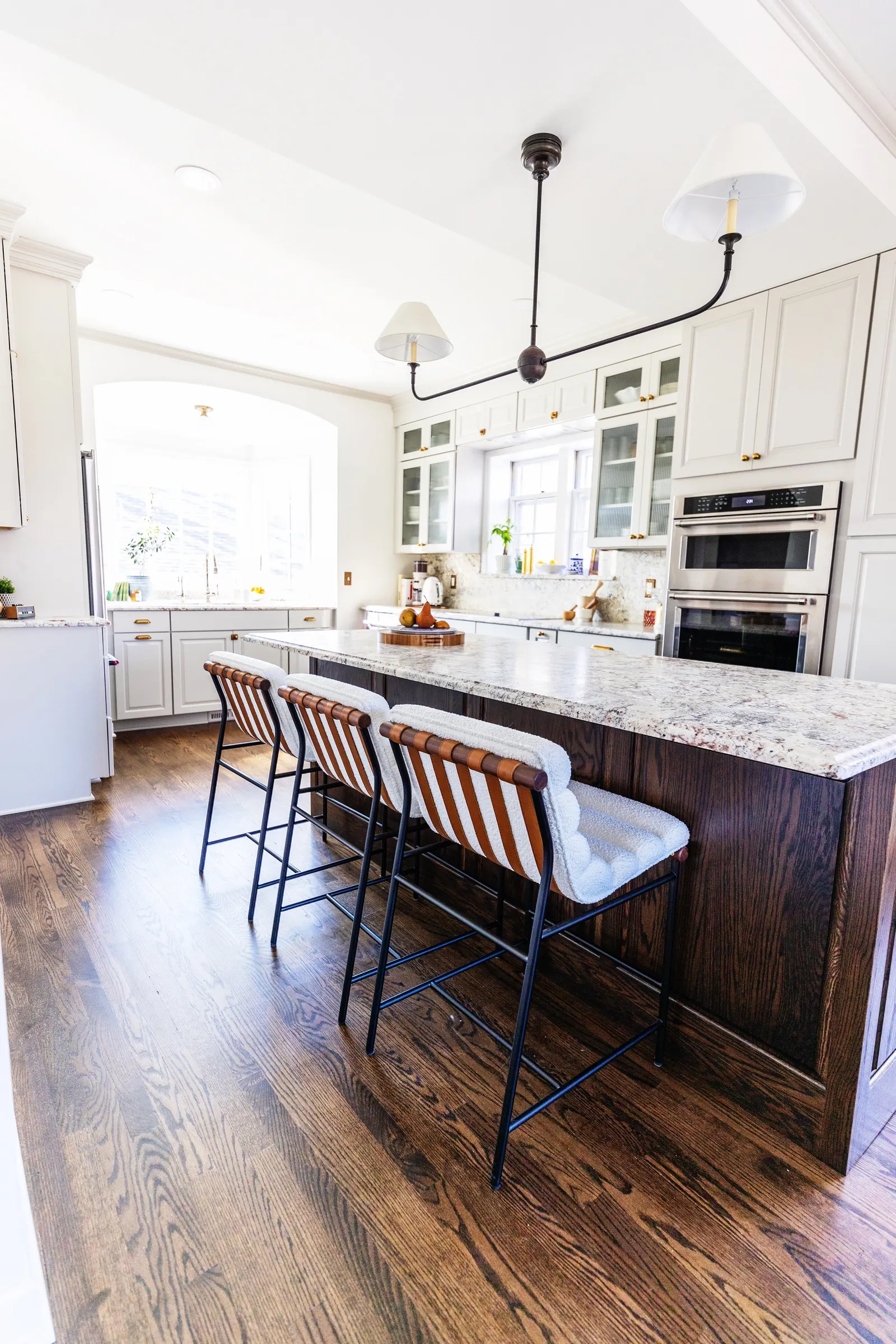 Modern kitchen with white cabinets, granite countertops, bar stools with striped cushions, and hardwood flooring.