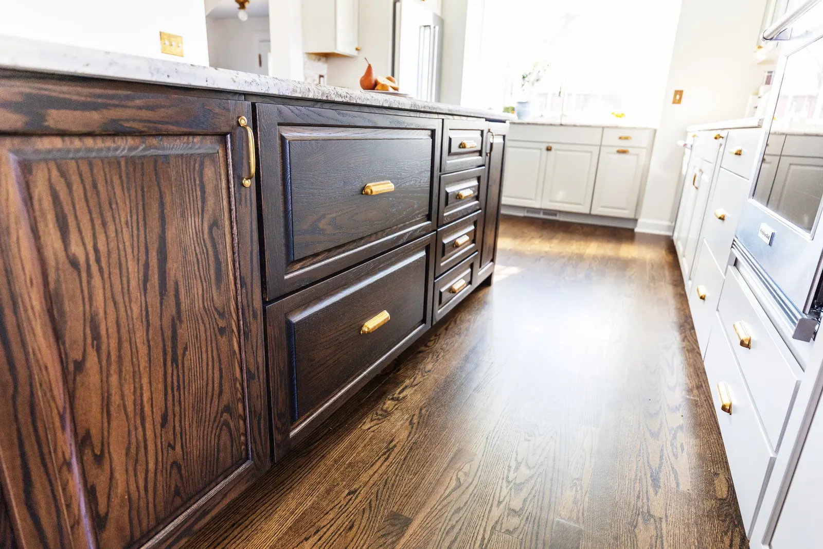 View of kitchen cabinets with dark wood and white finishes, gold hardware, and a laminate countertop in a bright kitchen with natural light.