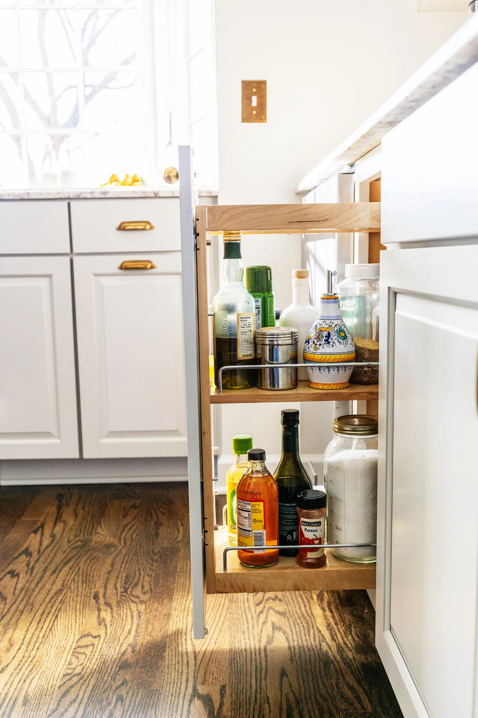 Open kitchen cabinet with shelves holding bottles, jars, and spices, near a stove and white cabinets.