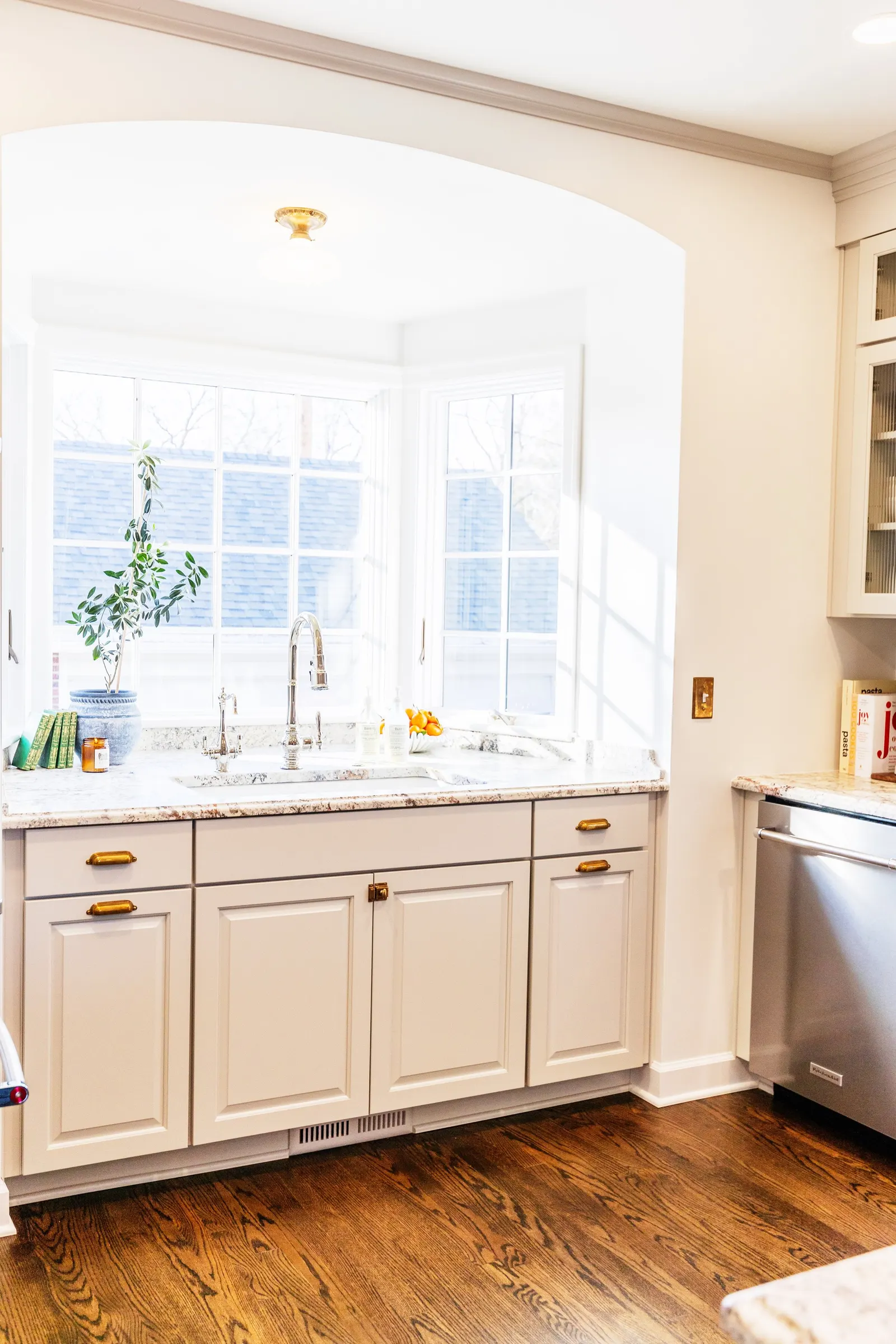 Bright kitchen with white cabinets, granite countertops, a stainless steel dishwasher, and a large window with a view of the outside, illuminated by sunlight.