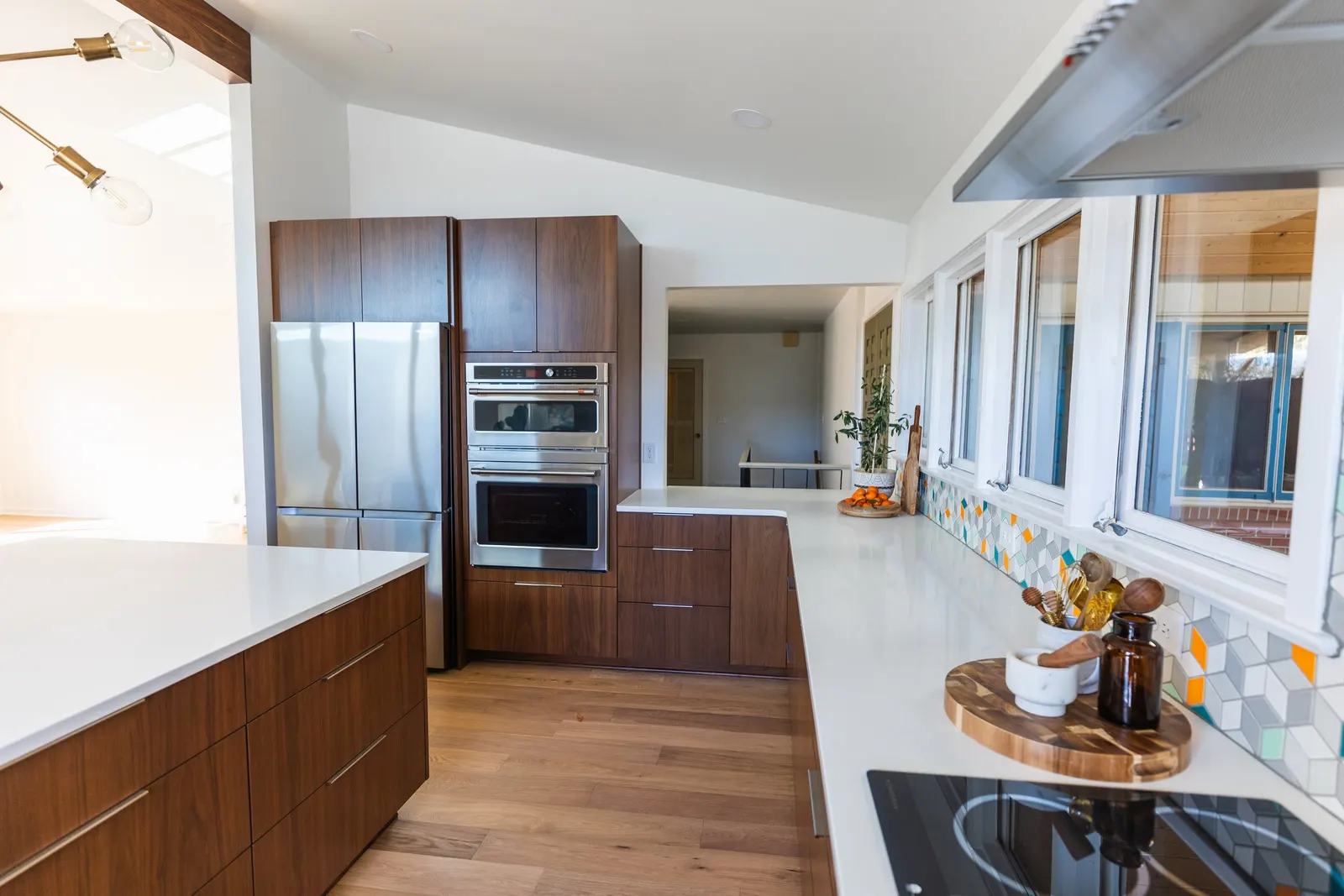 Modern kitchen with white countertops, wooden cabinets, stainless steel appliances, and a colorful tile backsplash.