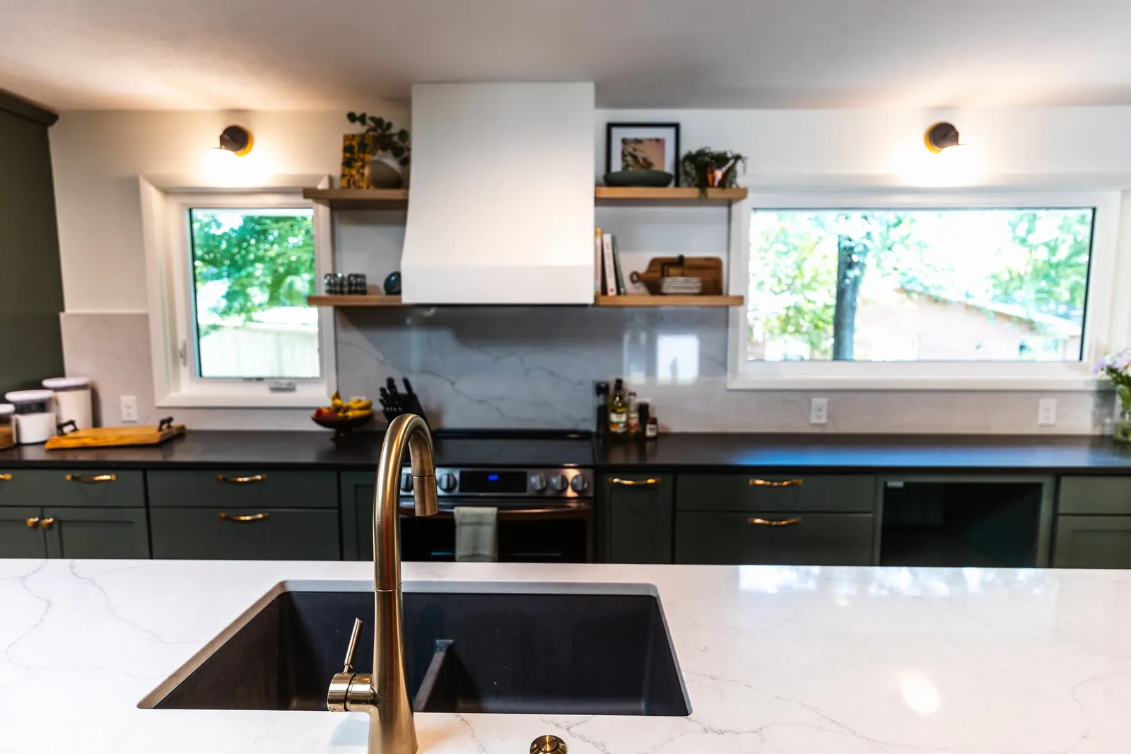 1962 Kitchen Remodel, dark green cabinets, white quartz island, wooden floors, brass hardware, wood cabinets, custom hood, floating shelves, dark countertops, open shelving, large windows.
