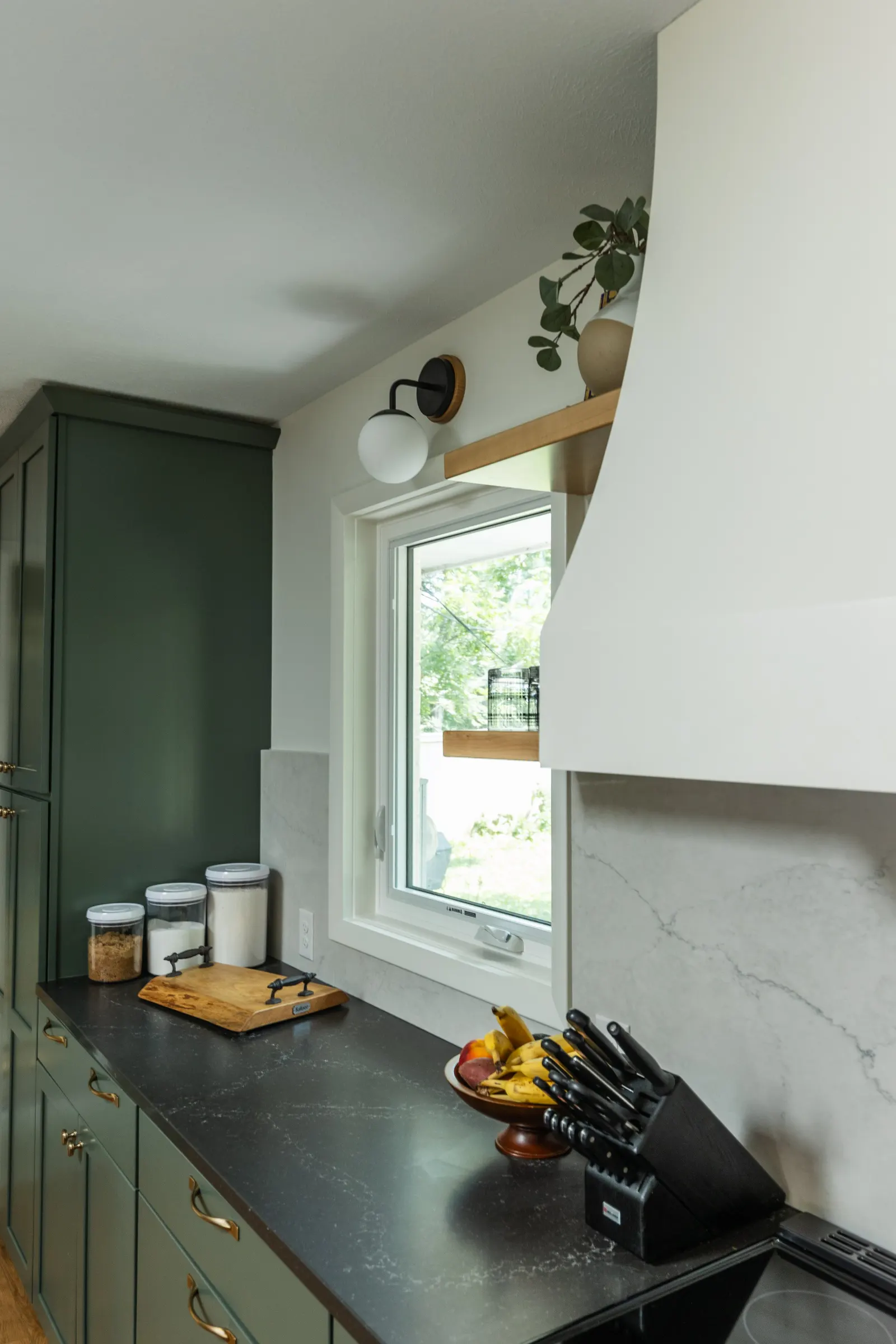1962 Kitchen Remodel, dark green cabinets, white quartz island, wooden floors, brass hardware, wood cabinets, custom hood, floating shelves, dark countertops, open shelving, large windows.