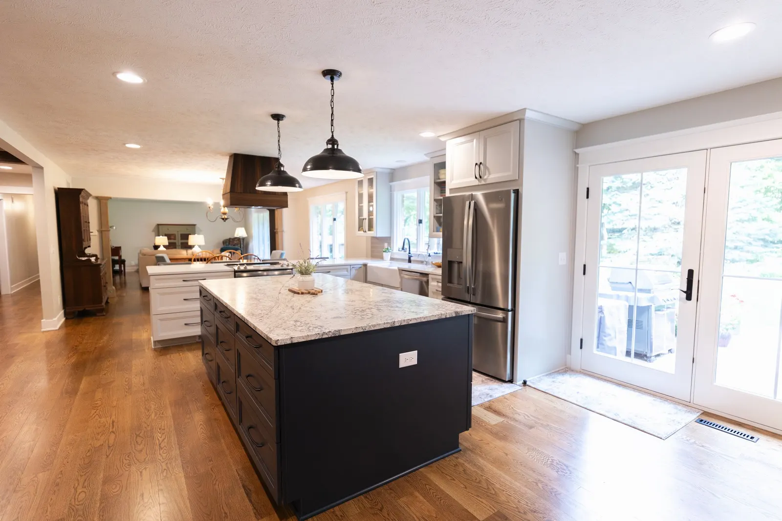 1974 Whole Home Remodel, kitchen remodel, wood floors, quartz countertop, craftsmanship, farmhouse style, custom hood, white cabinets, matte black hardware, farmhouse sink, pendant lights, large island, dual tone kitchen, large windows, patio doors.