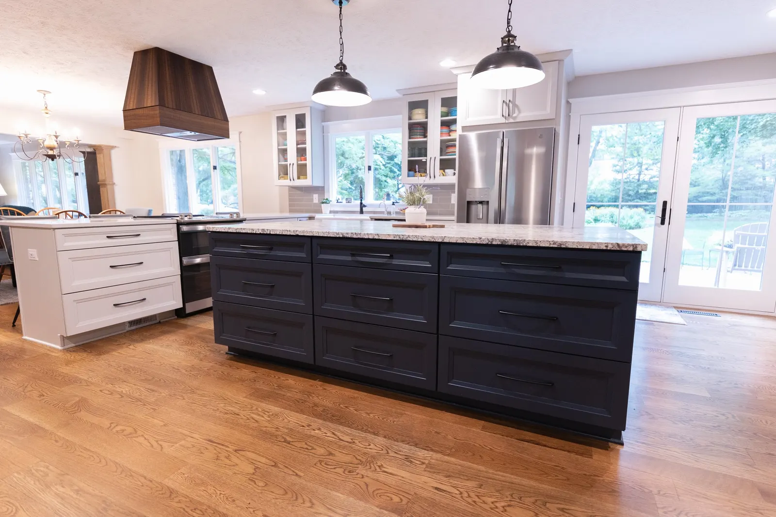 1974 Whole Home Remodel, kitchen remodel, wood floors, quartz countertop, craftsmanship, farmhouse style, custom hood, white cabinets, matte black hardware, farmhouse sink, pendant lights, large island, dual tone kitchen, large windows, patio doors.