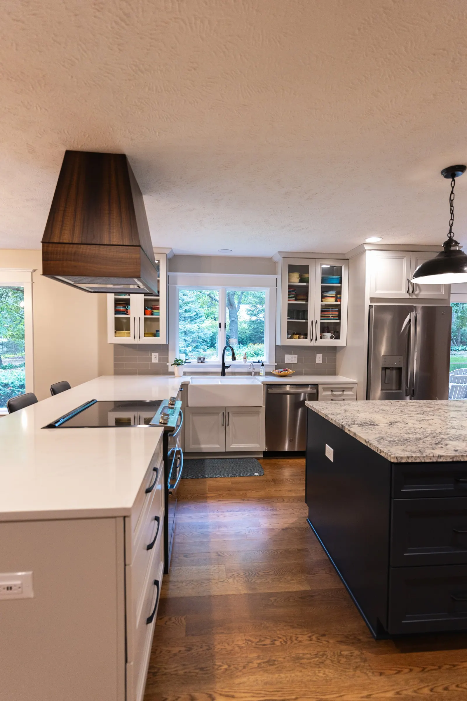 1974 Whole Home Remodel, kitchen remodel, wood floors, quartz countertop, craftsmanship, farmhouse style, custom hood, white cabinets, matte black hardware, farmhouse sink, pendant lights, large island, dual tone kitchen, large windows, patio doors.