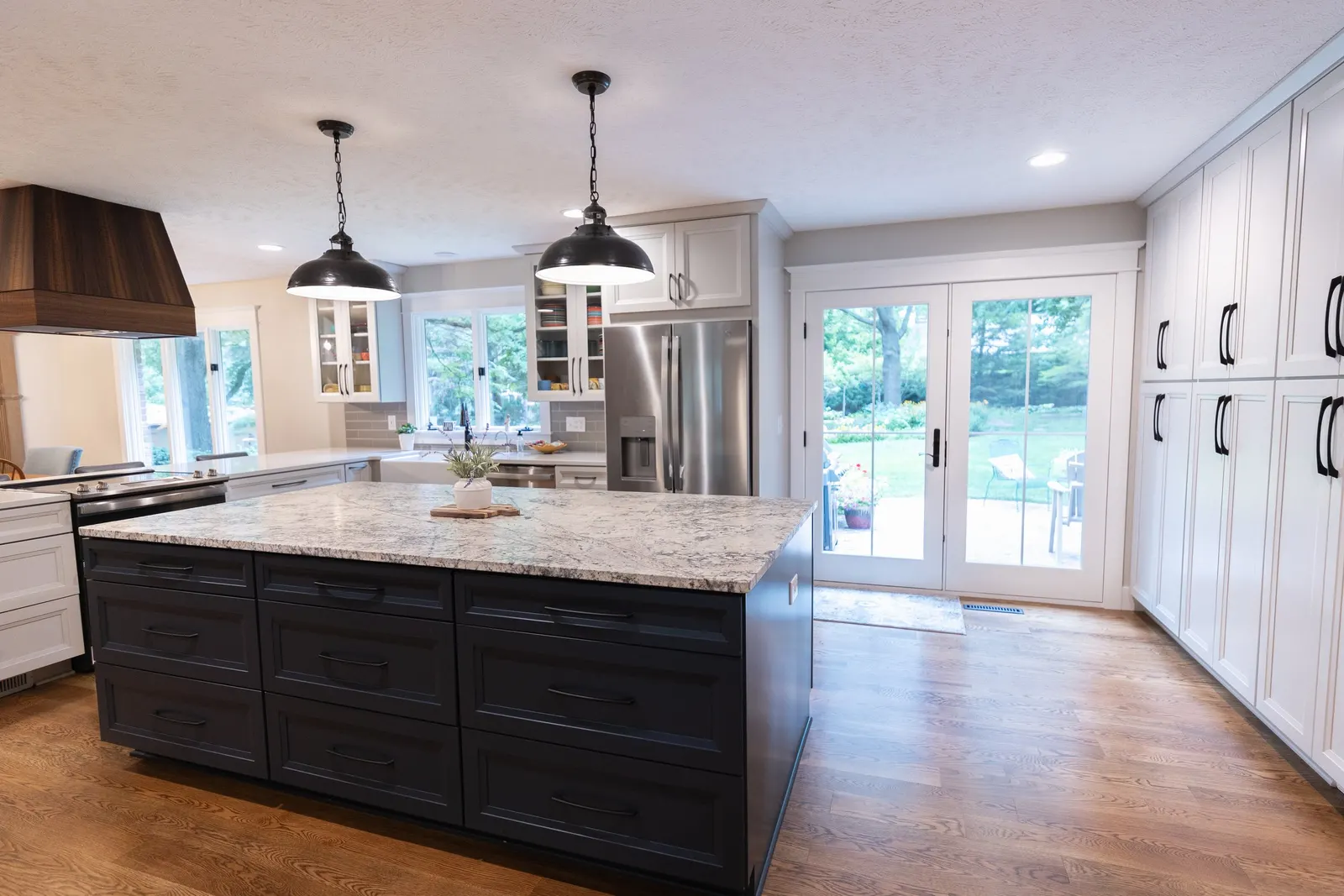 1974 Whole Home Remodel, kitchen remodel, wood floors, quartz countertop, craftsmanship, farmhouse style, custom hood, white cabinets, matte black hardware, farmhouse sink, pendant lights, large island, dual tone kitchen, large windows, patio doors.