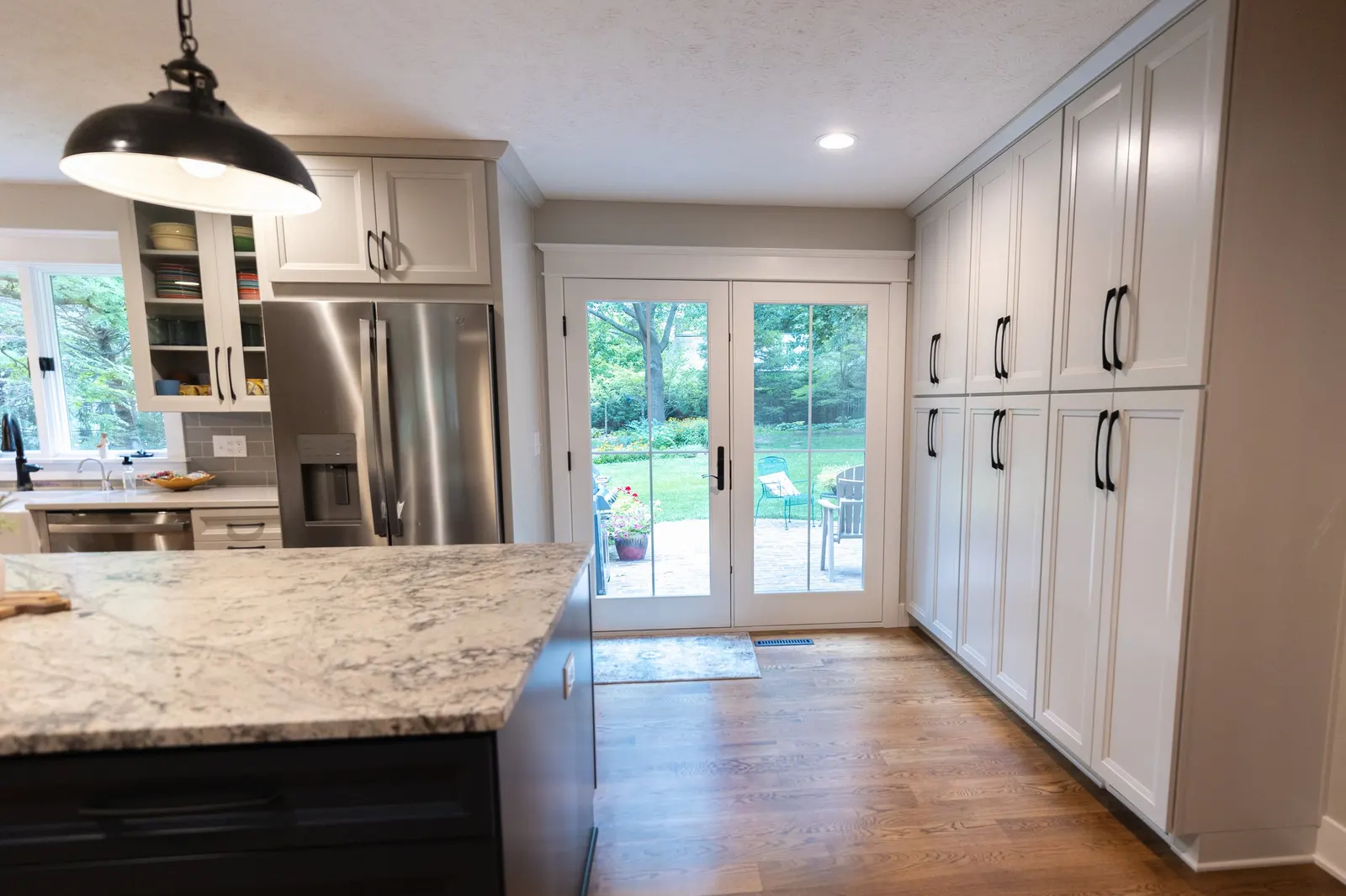 1974 Whole Home Remodel, kitchen remodel, wood floors, quartz countertop, craftsmanship, farmhouse style, custom hood, white cabinets, matte black hardware, farmhouse sink, pendant lights, large island, dual tone kitchen, large windows, patio doors.
