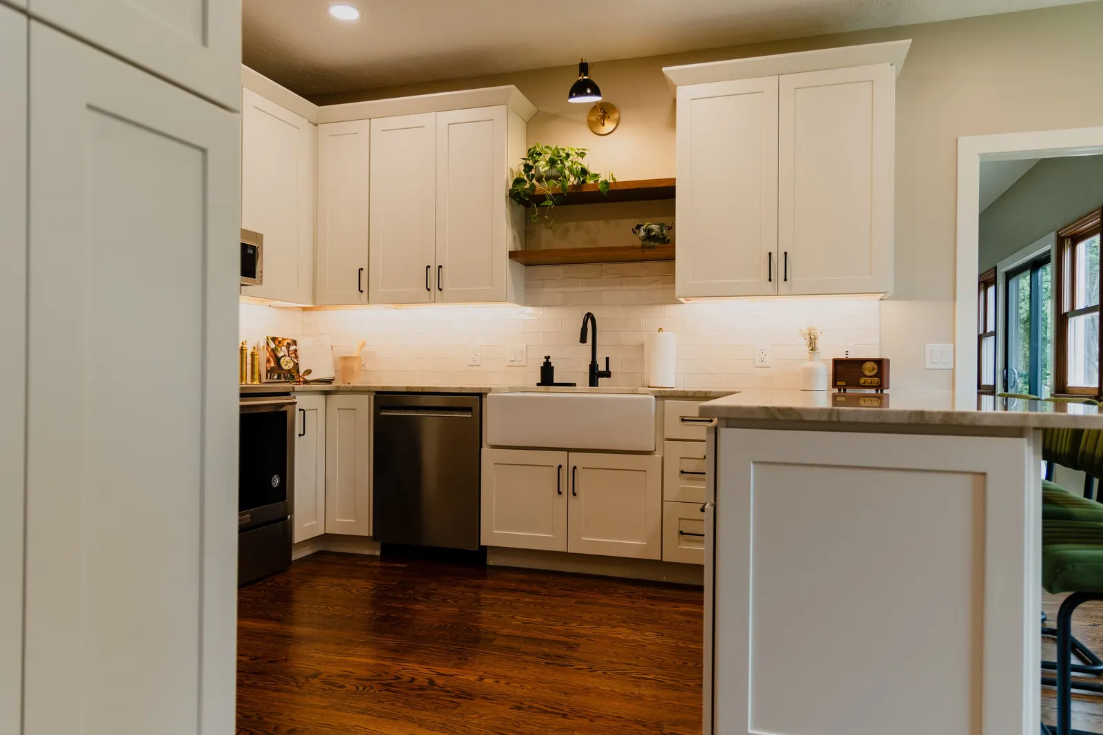 Kitchen with white cabinets, a black faucet and sink, wooden open shelves, and hardwood floors.