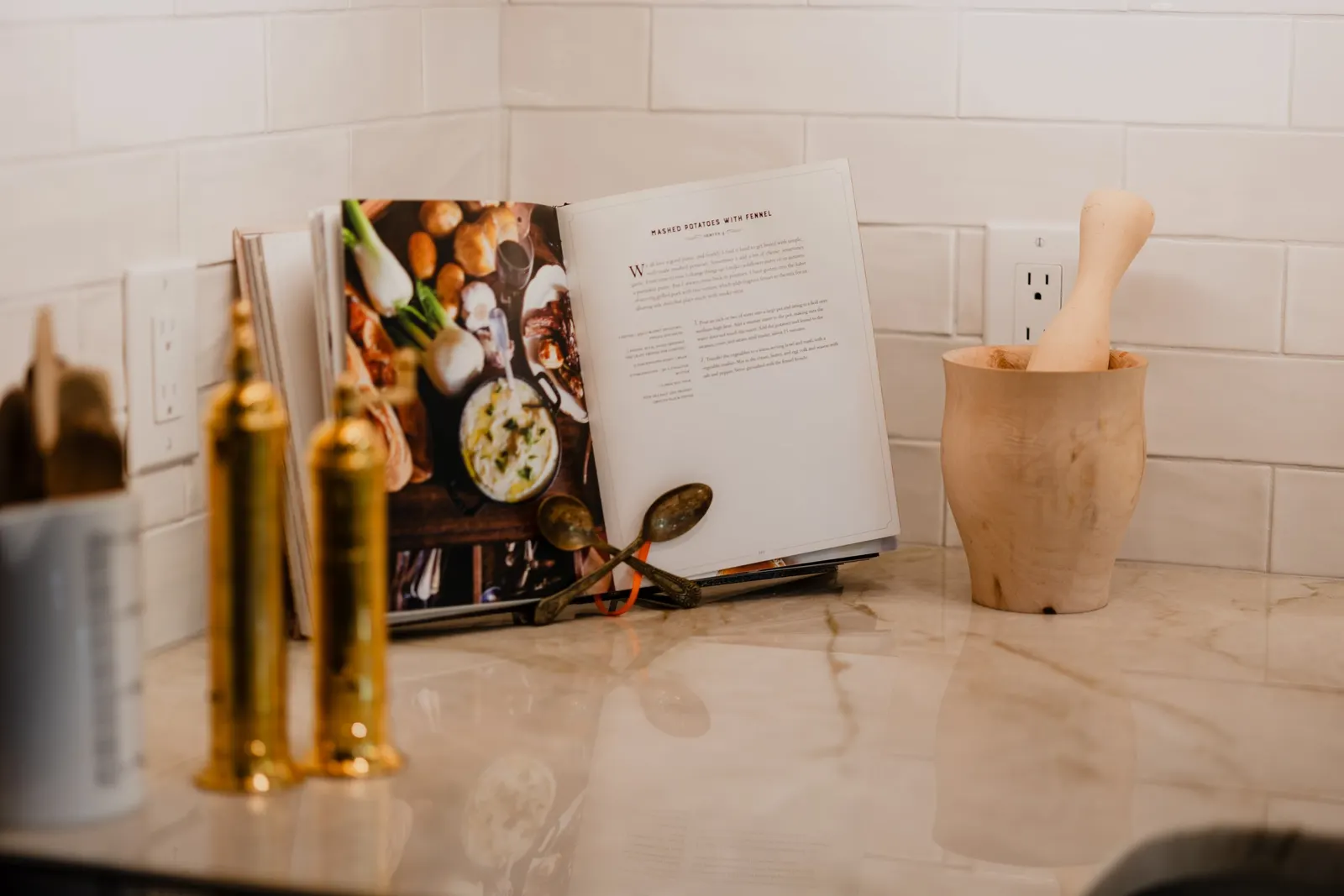 Open cookbook and mortar with pestle on kitchen counter with spice bottles. 1935 Kitchen Remodel. White Subway Backsplash. Quartz Countertop.