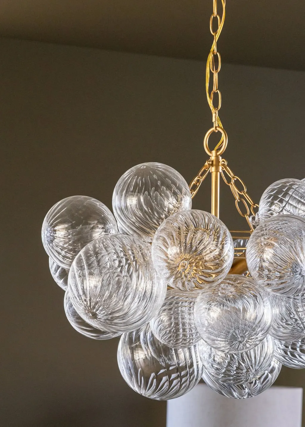A chandelier made of clear glass globes with swirling patterns, hanging from a gold chain and support.