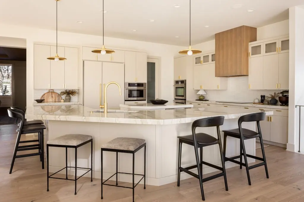 Modern kitchen with white cabinets, marble island, black chairs, and gold accents.