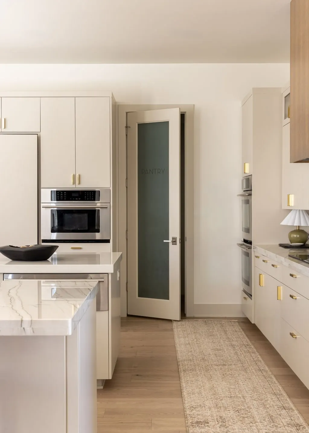 Modern kitchen with white cabinets, marble countertops, built-in double oven, and pantry door labeled 'PANTY'