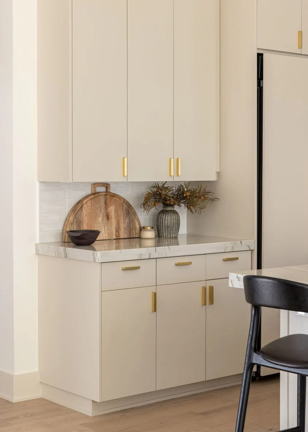 A kitchen corner with white cabinets and gold handles, a marble countertop, a wooden tray, a bowl, and a vase with dried flowers.