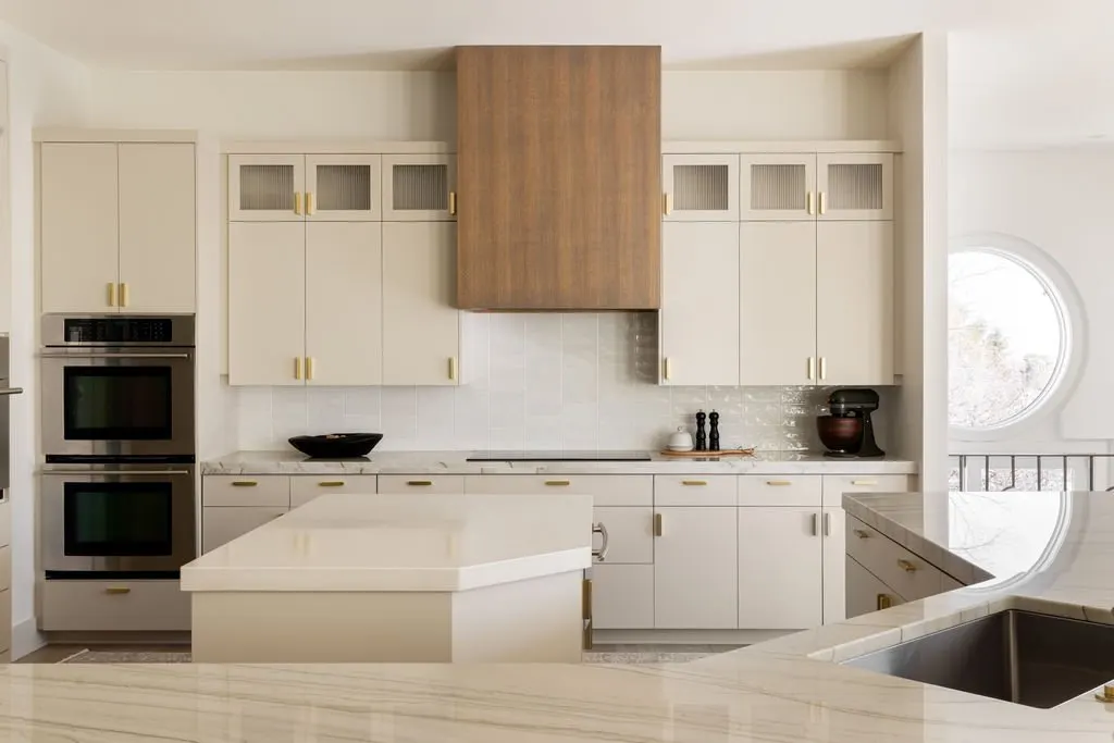 Modern kitchen with white cabinets, a built-in double oven on the left, a cooktop with a wooden range hood, and a curved marble countertop