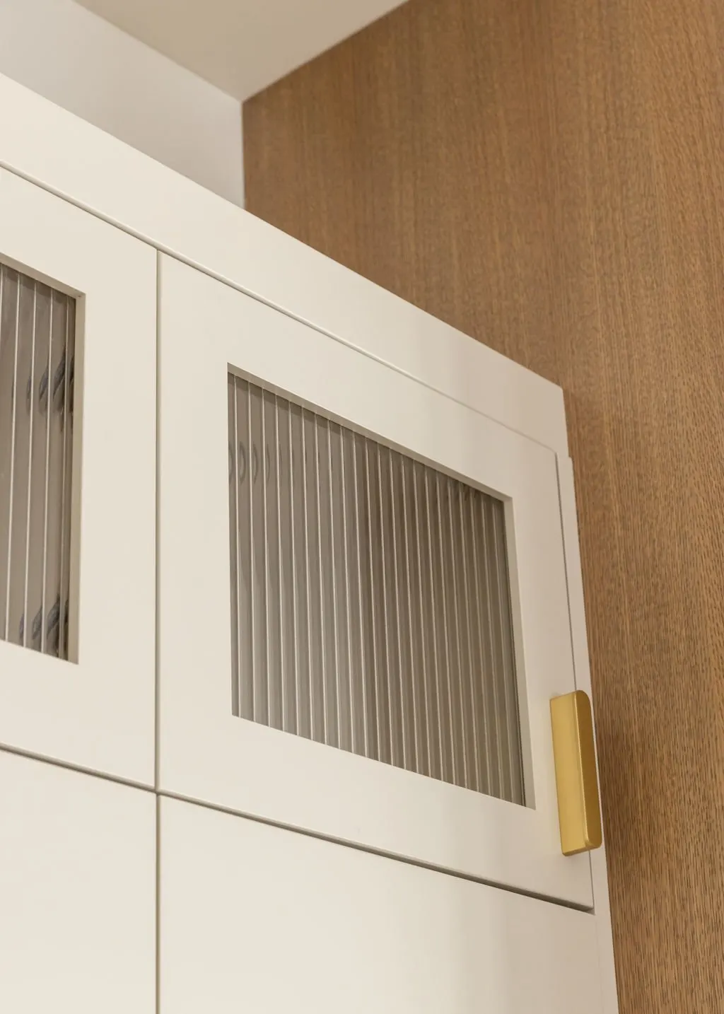 Close-up of a white cabinet with glass-paneled doors and vertical metal strips, against a brown textured wall.