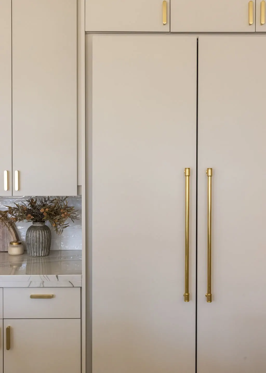 Close-up of a modern kitchen cabinet with gold handles, a marble countertop with a vase of dried flowers, and part of a drawer.