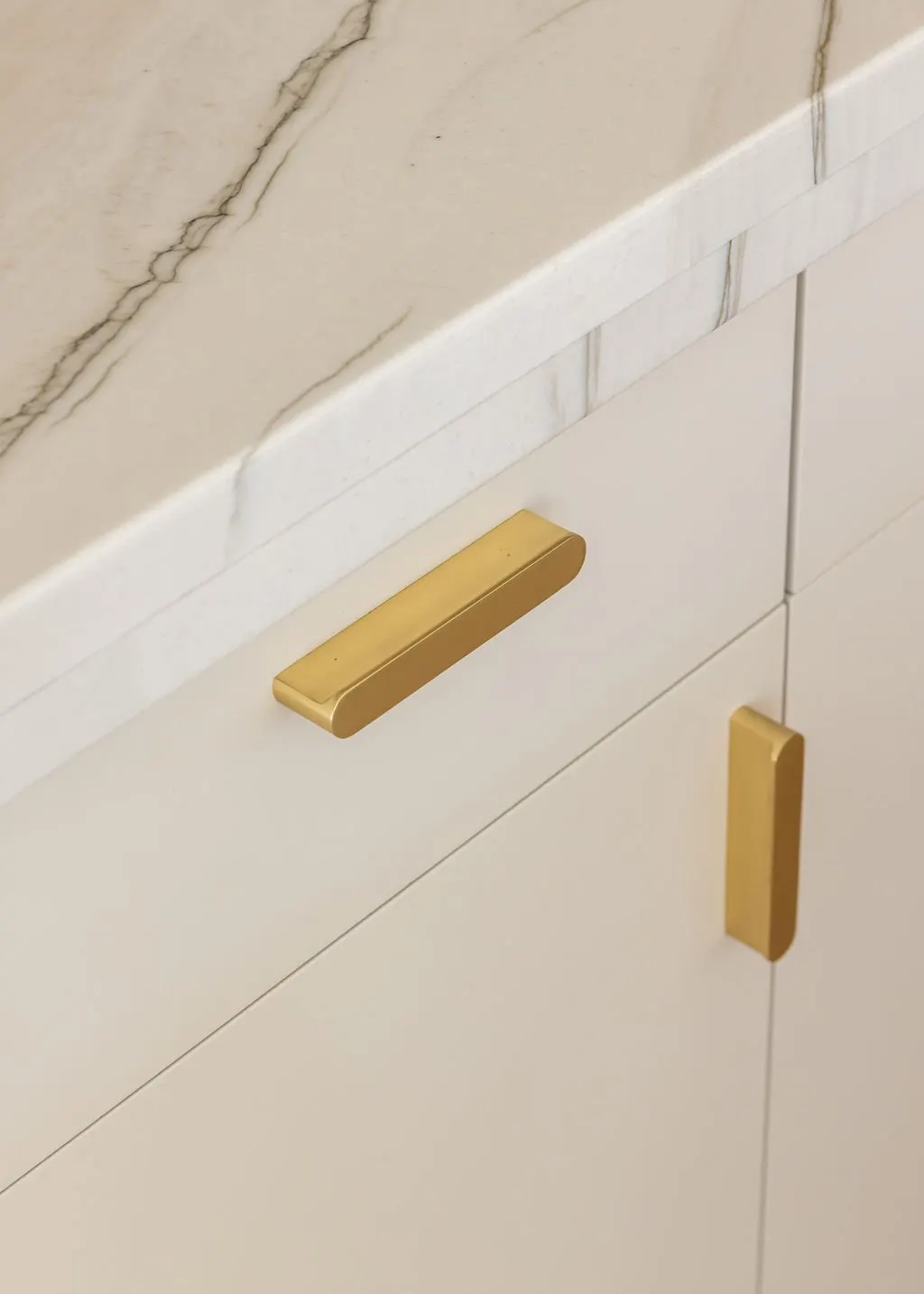 Close-up of a cream-colored cabinet with gold handles and a marble countertop.