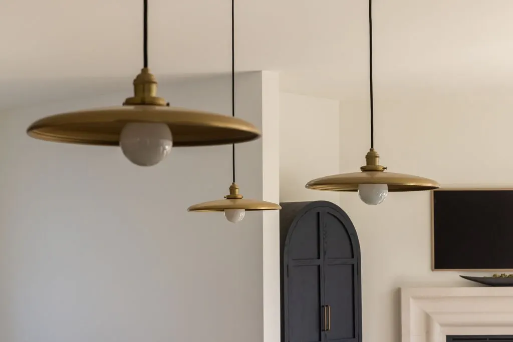 Three hanging ceiling lights with brass fixtures and white bulbs in a room with white walls, a black arched cabinet, and a black flat-screen television.