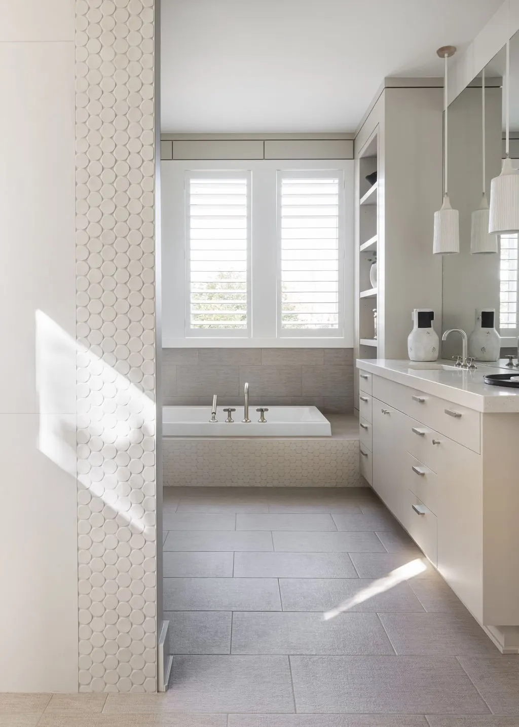 Modern white bathroom with large window, bathtub, and vanity with mirror and decorative vases.