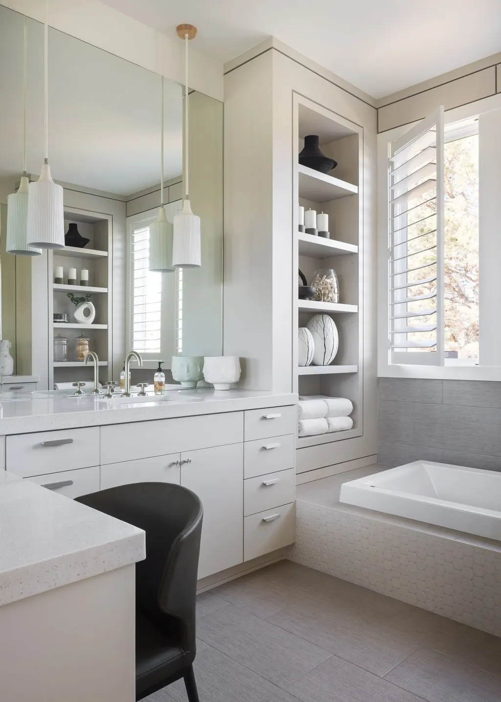 Modern bathroom with white cabinetry, a large mirror, open shelving with decorative items and towels, a bathtub, and a window with plantation shutters.