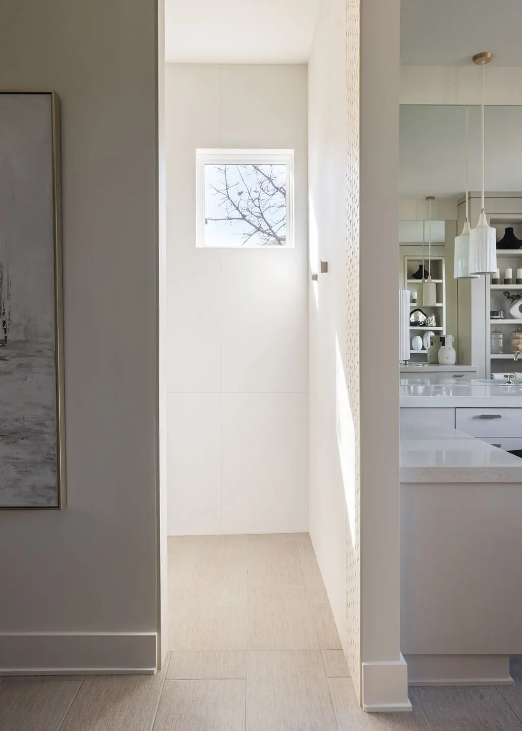 A modern, minimalistic kitchen with white cabinetry, open shelves displaying dishes, and a small window showing tree branches outside.