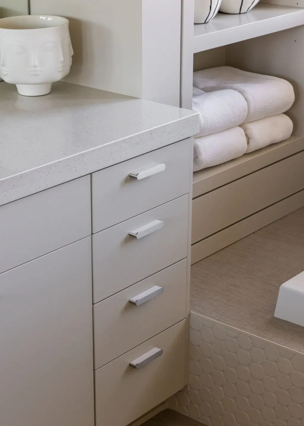 White bathroom vanity with drawers, a white countertop, and shelves with neatly folded white towels and decorative bowls.