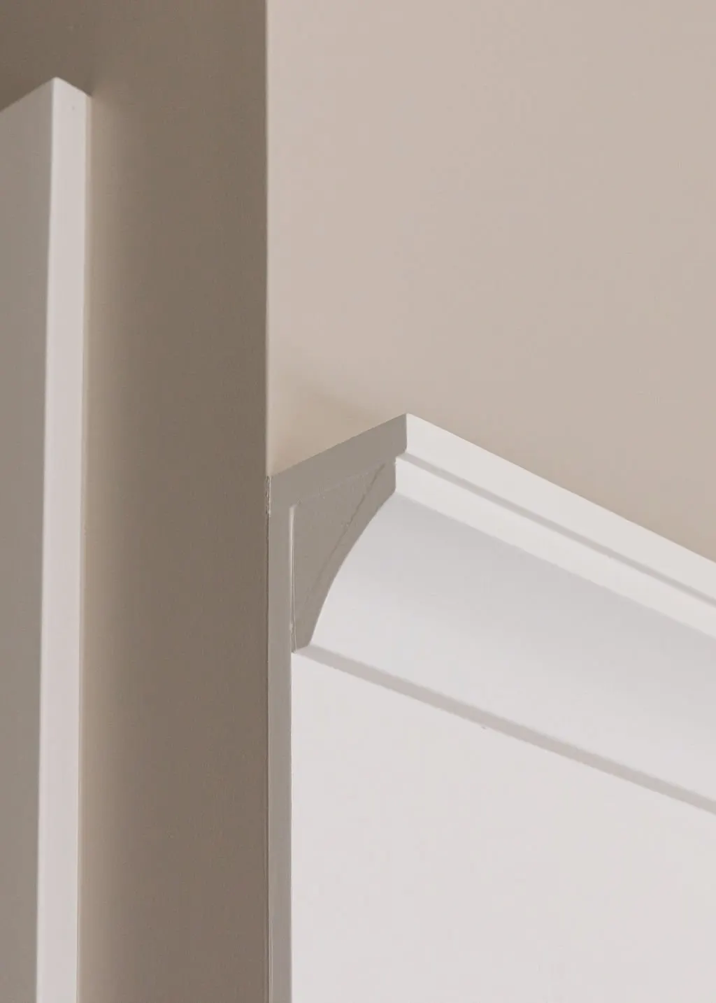 Close-up of a corner where a beige wall, a white door frame, and white crown molding meet.