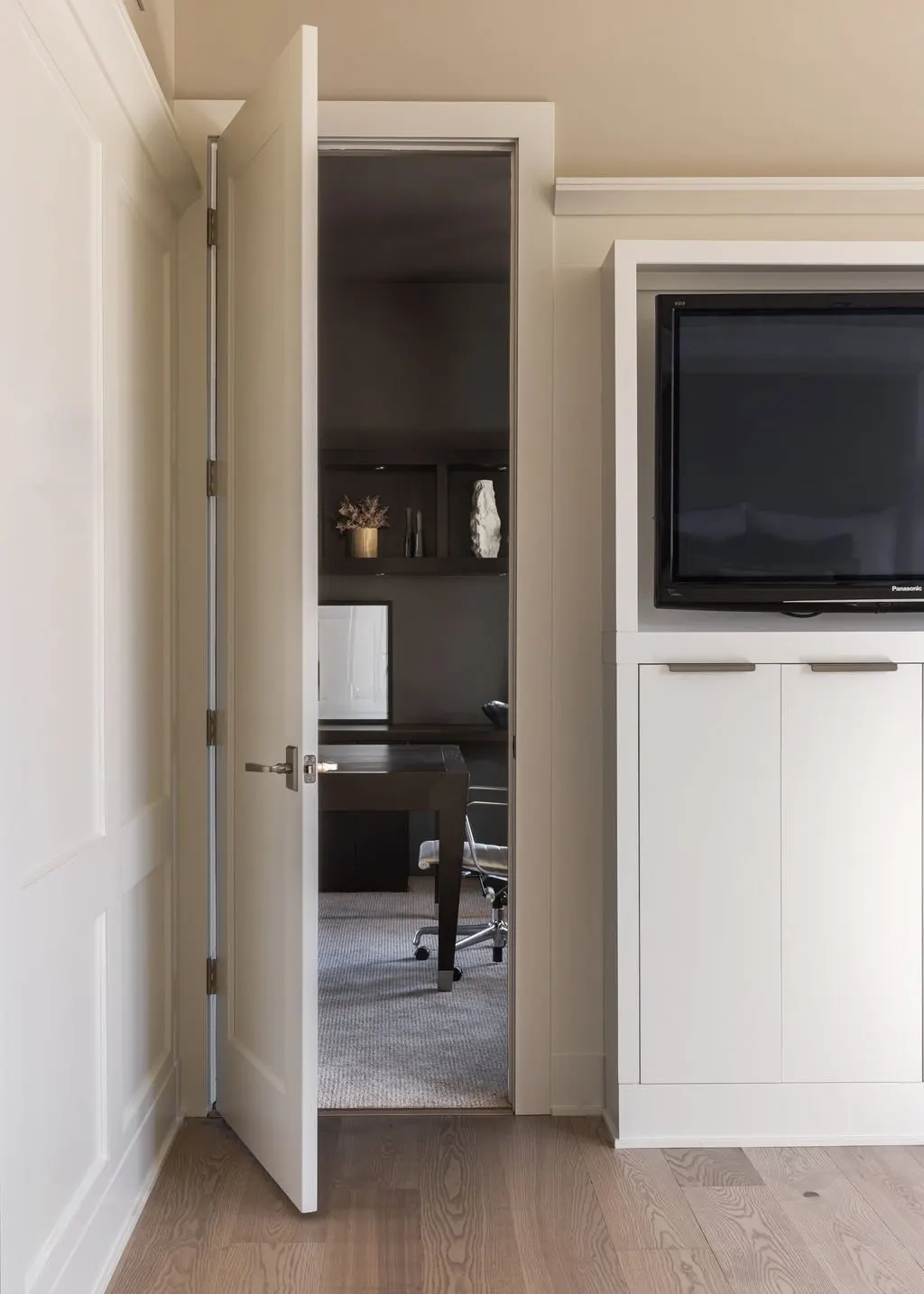 Open door showing a home office with a desk, chair, and decorative items on shelves inside.