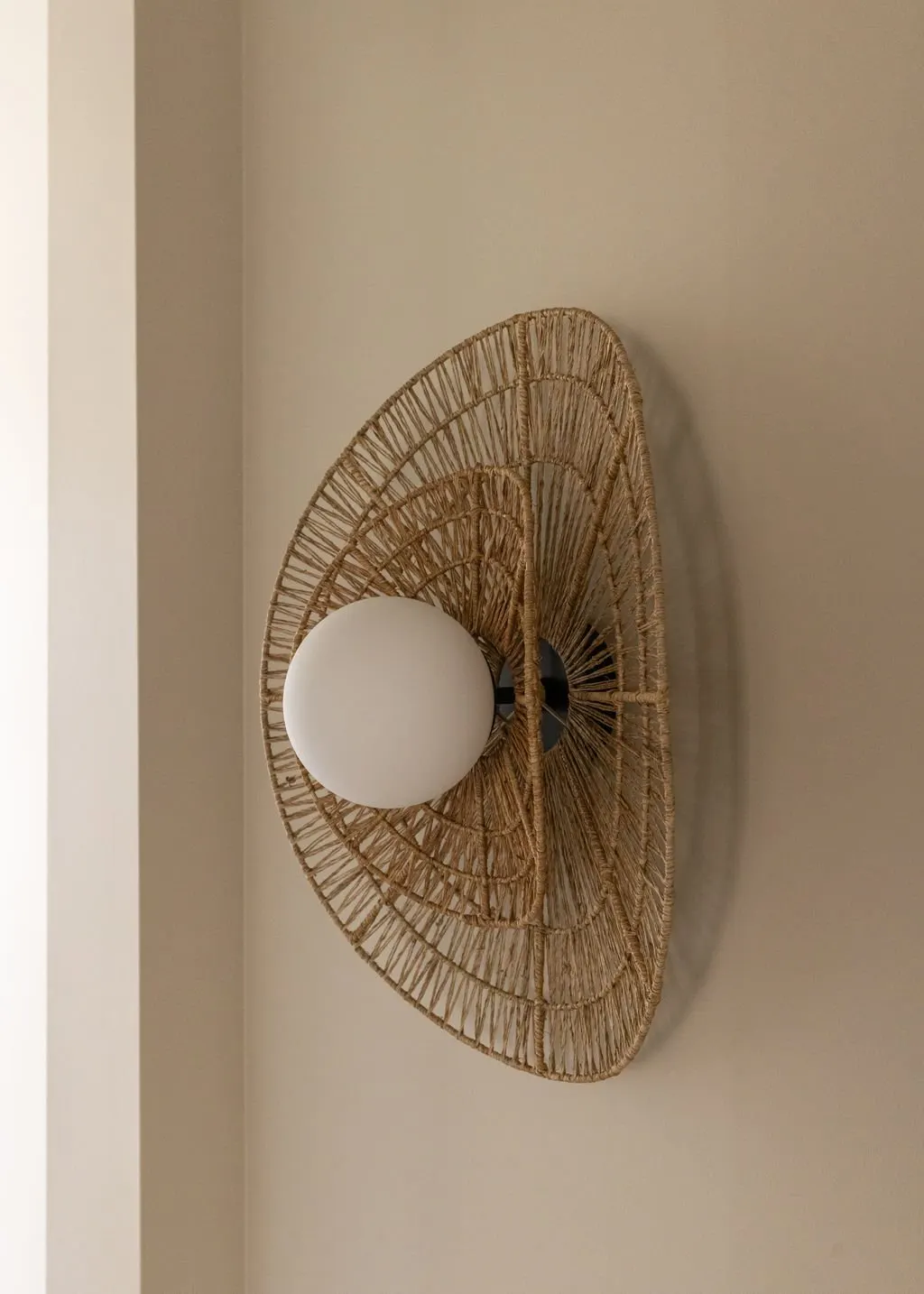 A ceiling light with a round white bulb inside a wicker lampshade in a room with beige walls.