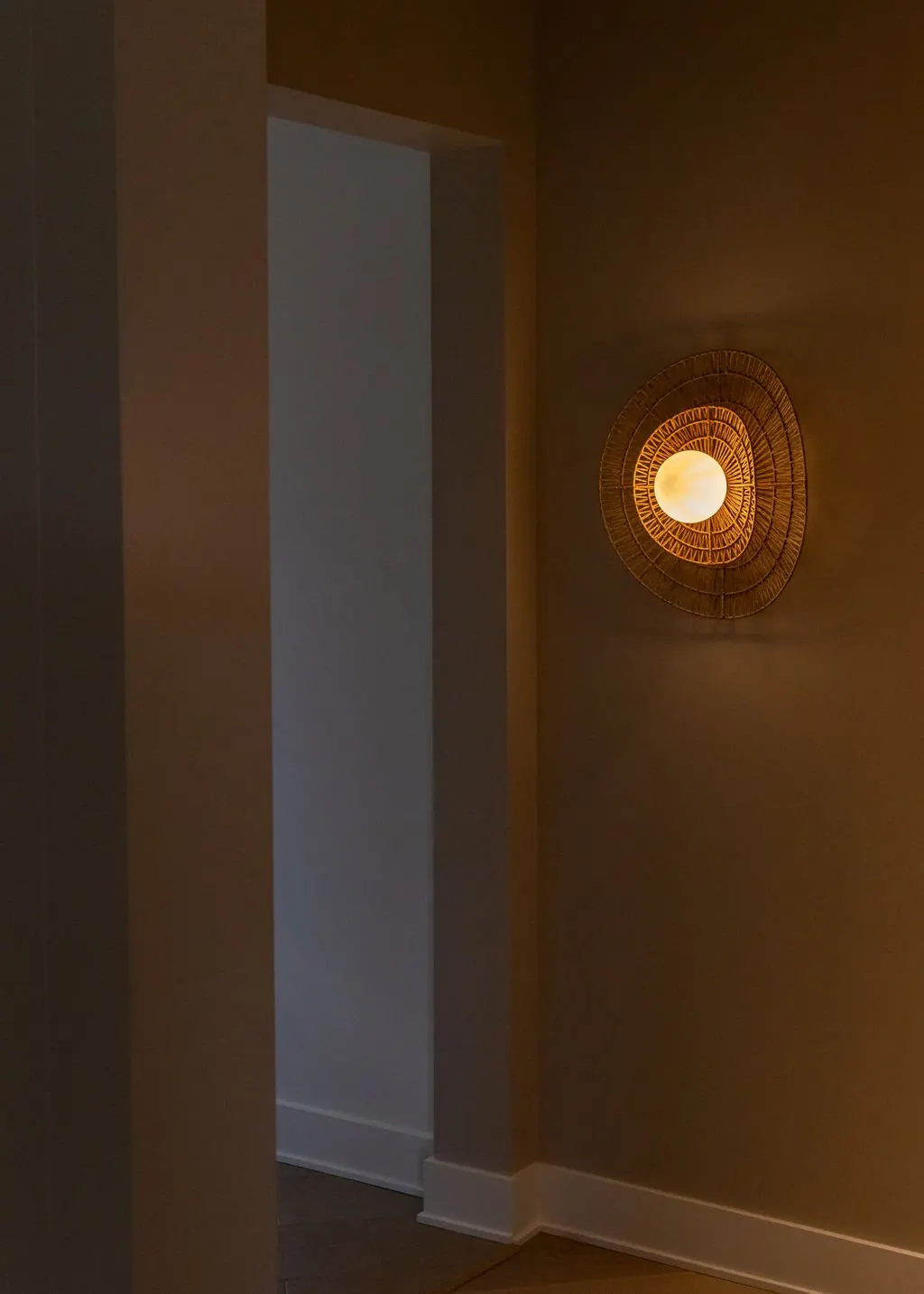 Wall-mounted circular light fixture with a woven design, emitting warm light in a corner of a room.