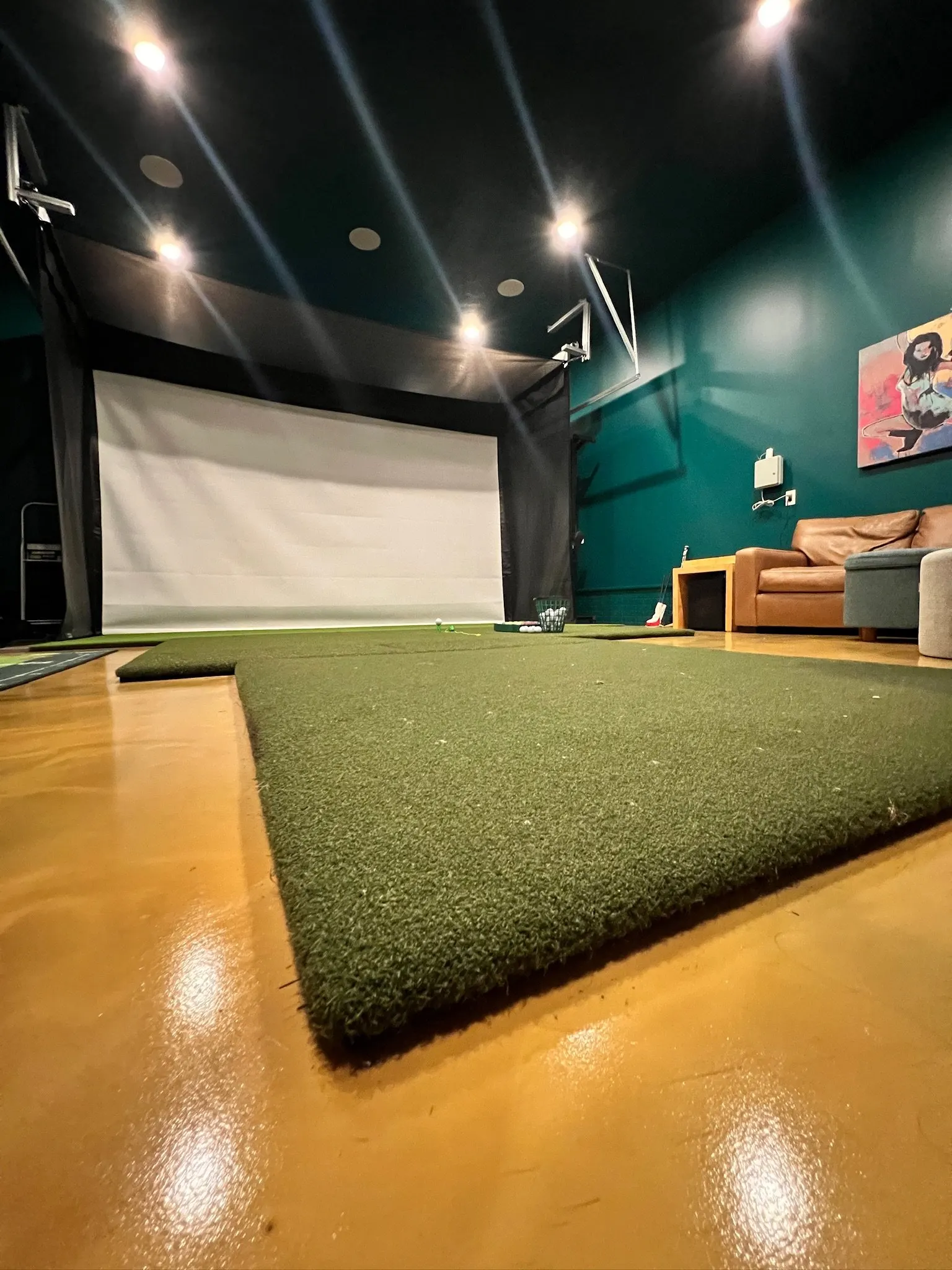Indoor golf simulator room with a large golf mat, a space for hitting golf balls, and a screen for virtual golf courses.