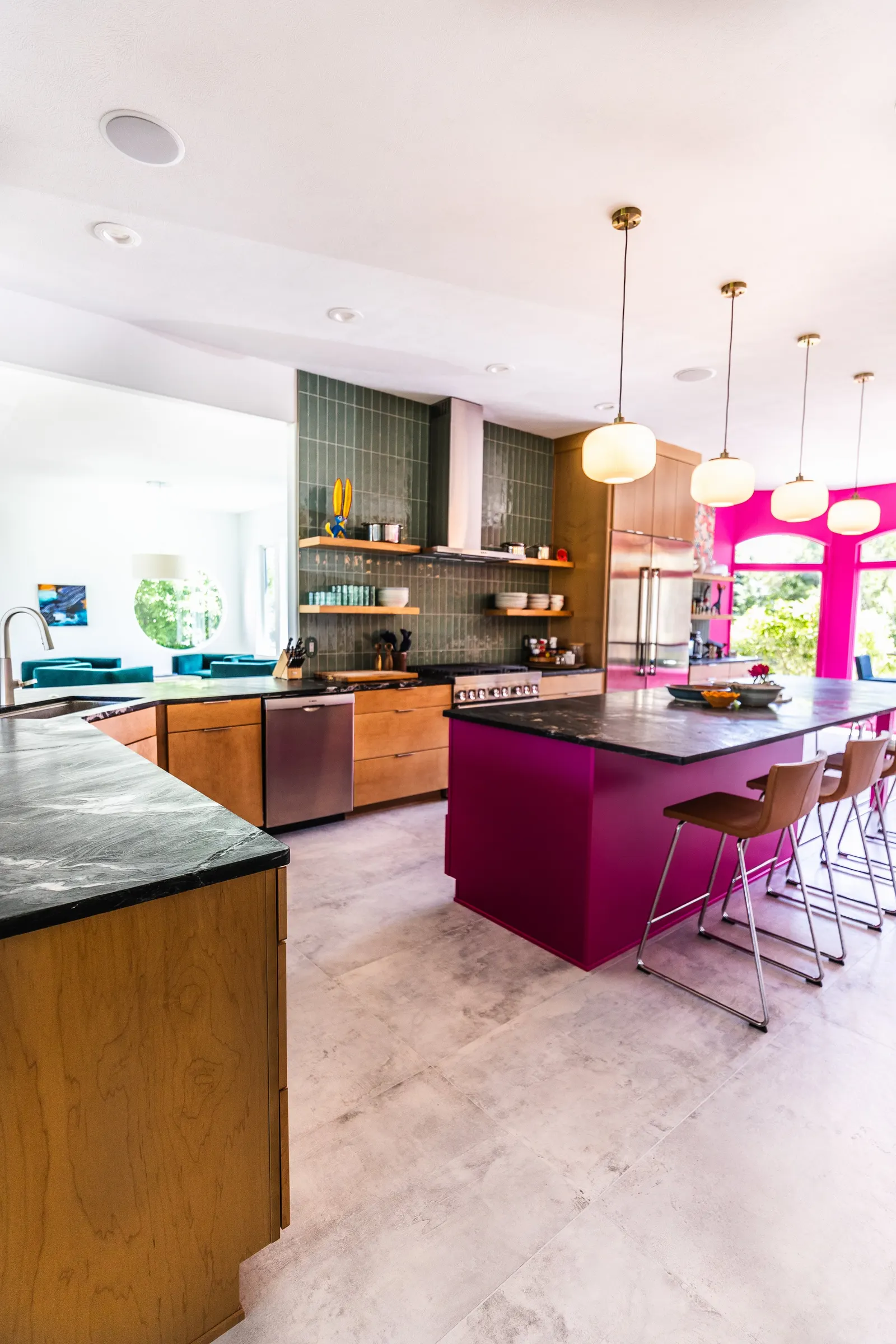 Modern kitchen with pink island, white bar stools, green tiled wall, and pendant lighting.
